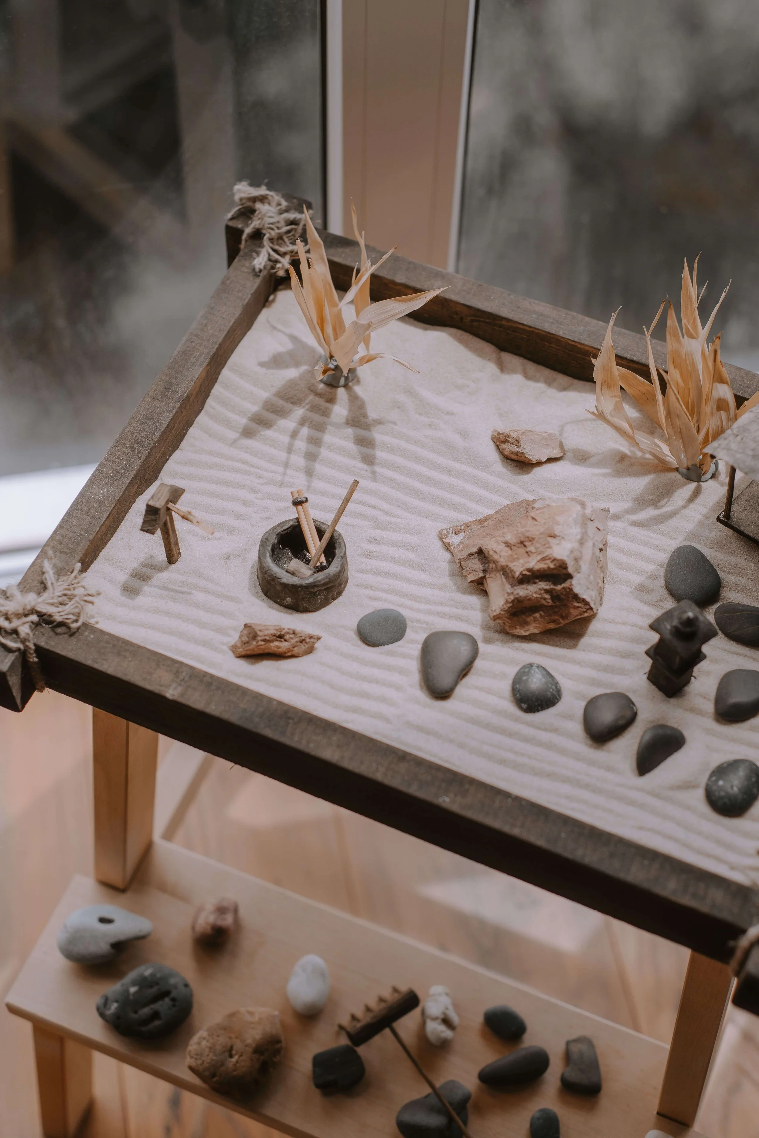 A sandtray display of rocks, stones, and small artifacts arranged on a tabletop, with some plants and decorative objects.