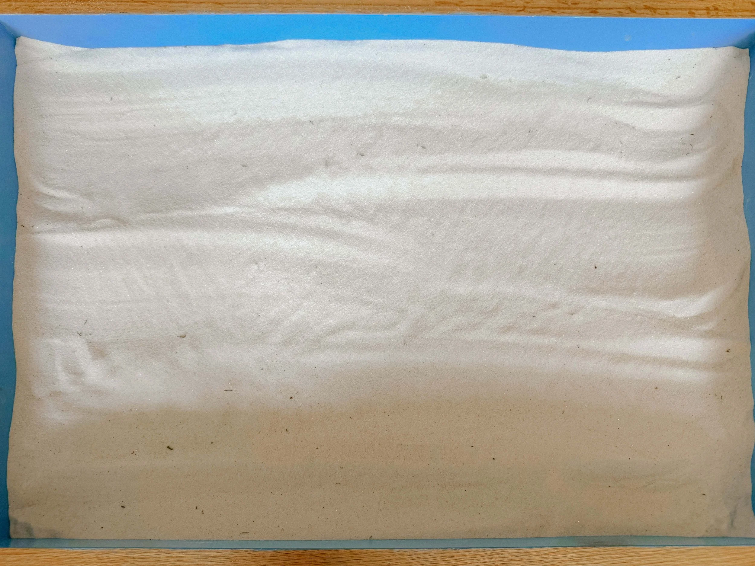 A rectangular sheet of white foam or sponge material placed on a blue background, with a wooden edge visible at the top.
