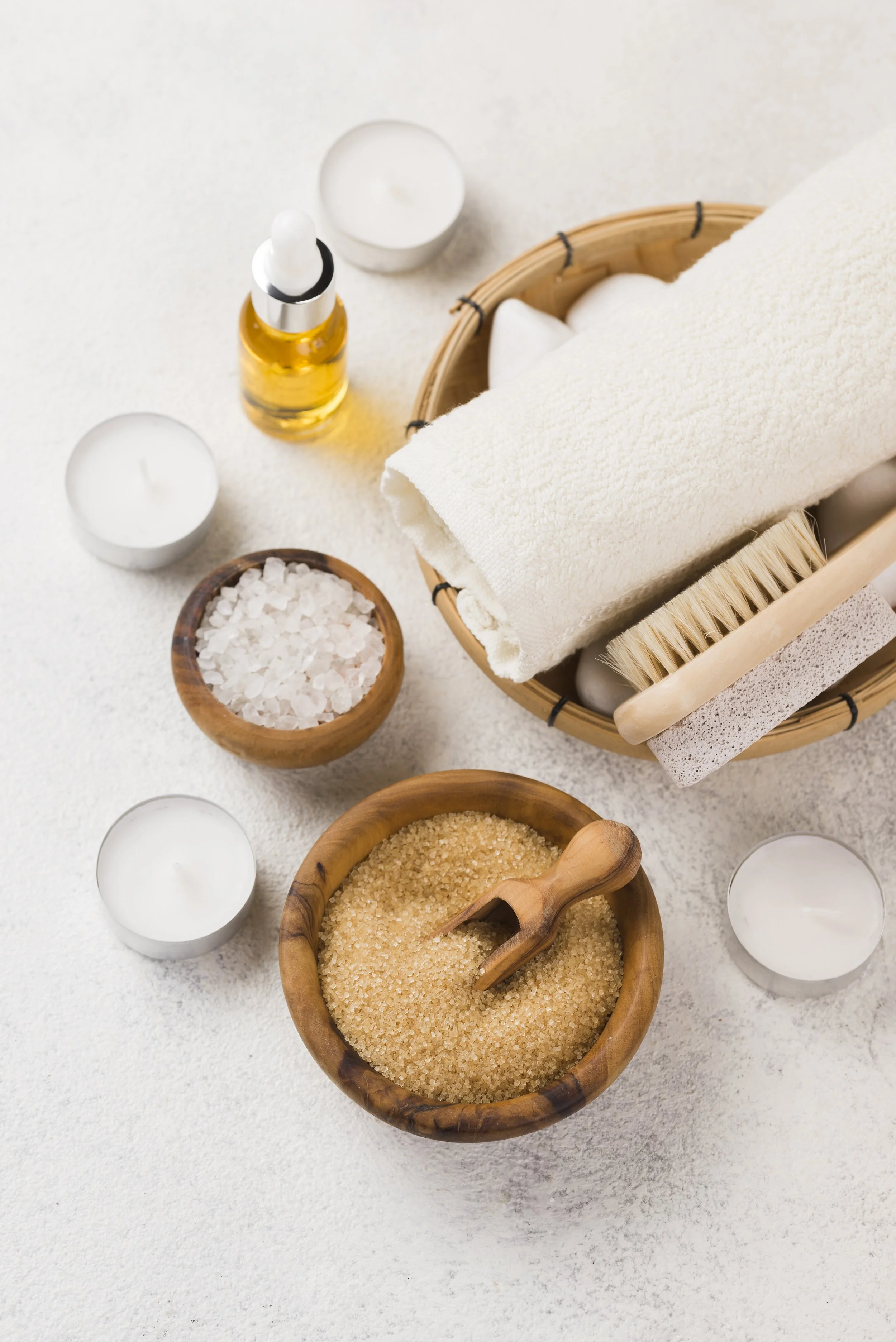 Des bougies blanches, un flacon d'huile essentielle, un brosse, des sels de bain, et un tapis blanc dans une ambiance spa ou bien-être.
