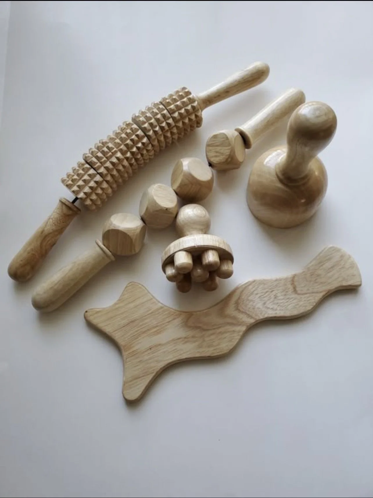 Un ensemble d'outils en bois, y compris un rouleau à pâtisserie, des formes géométriques, une poignée rotative, une spatule en bois, et une forme de poisson, disposés sur fond blanc.