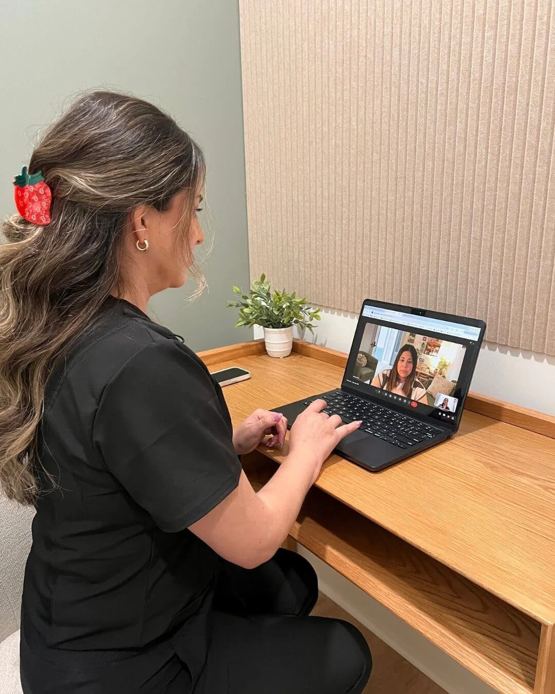 Nutritionist in black scrubs taking a virtual call on her laptop inside a phone booth
