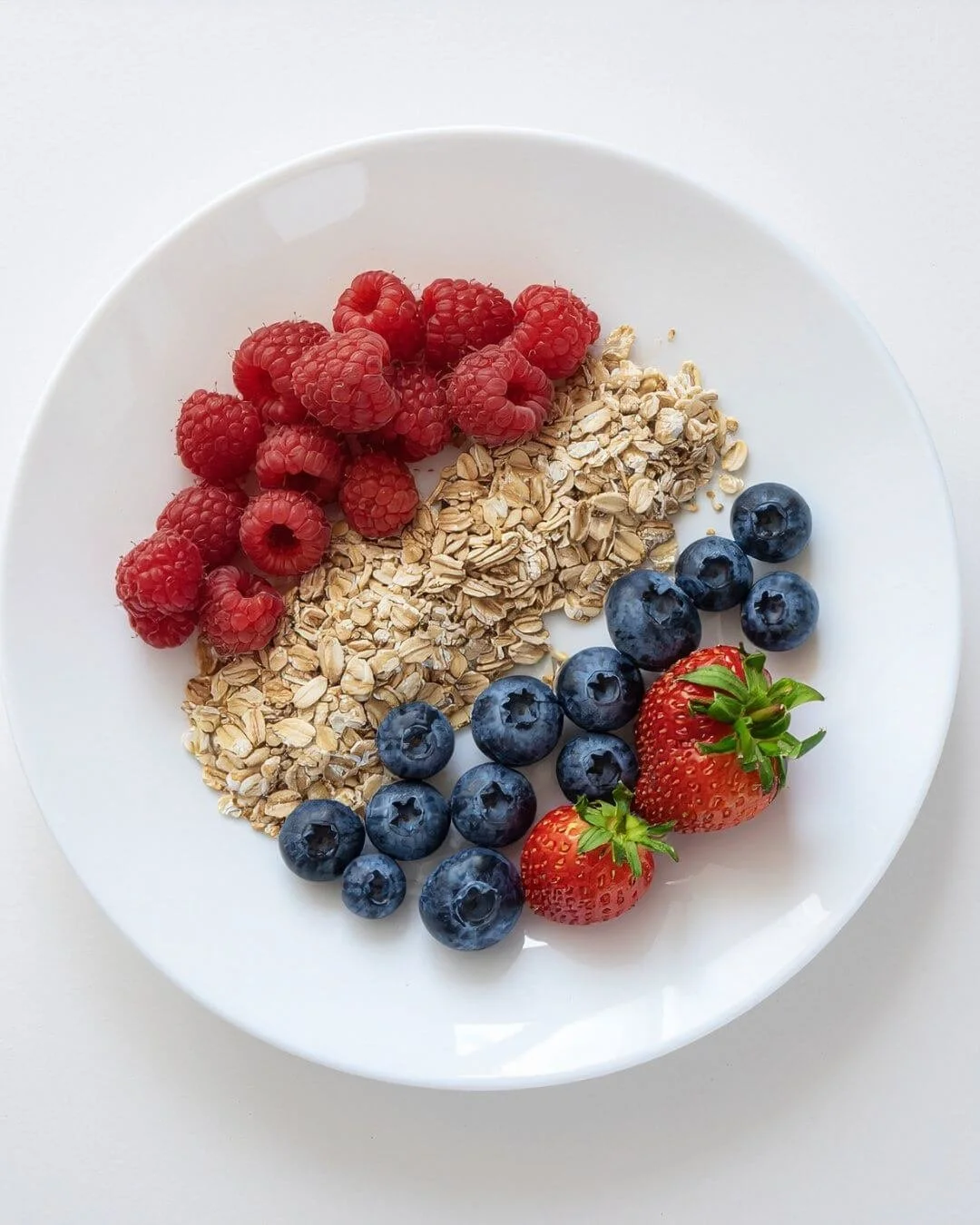 A white plate with raspberries, rolled oats, blueberries, and strawberries arranged on it.