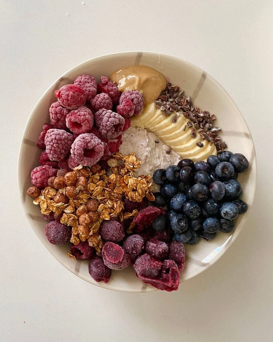 Healthy smoothie bowl featuring red berries, bananas, peanut butter, blueberries, granola