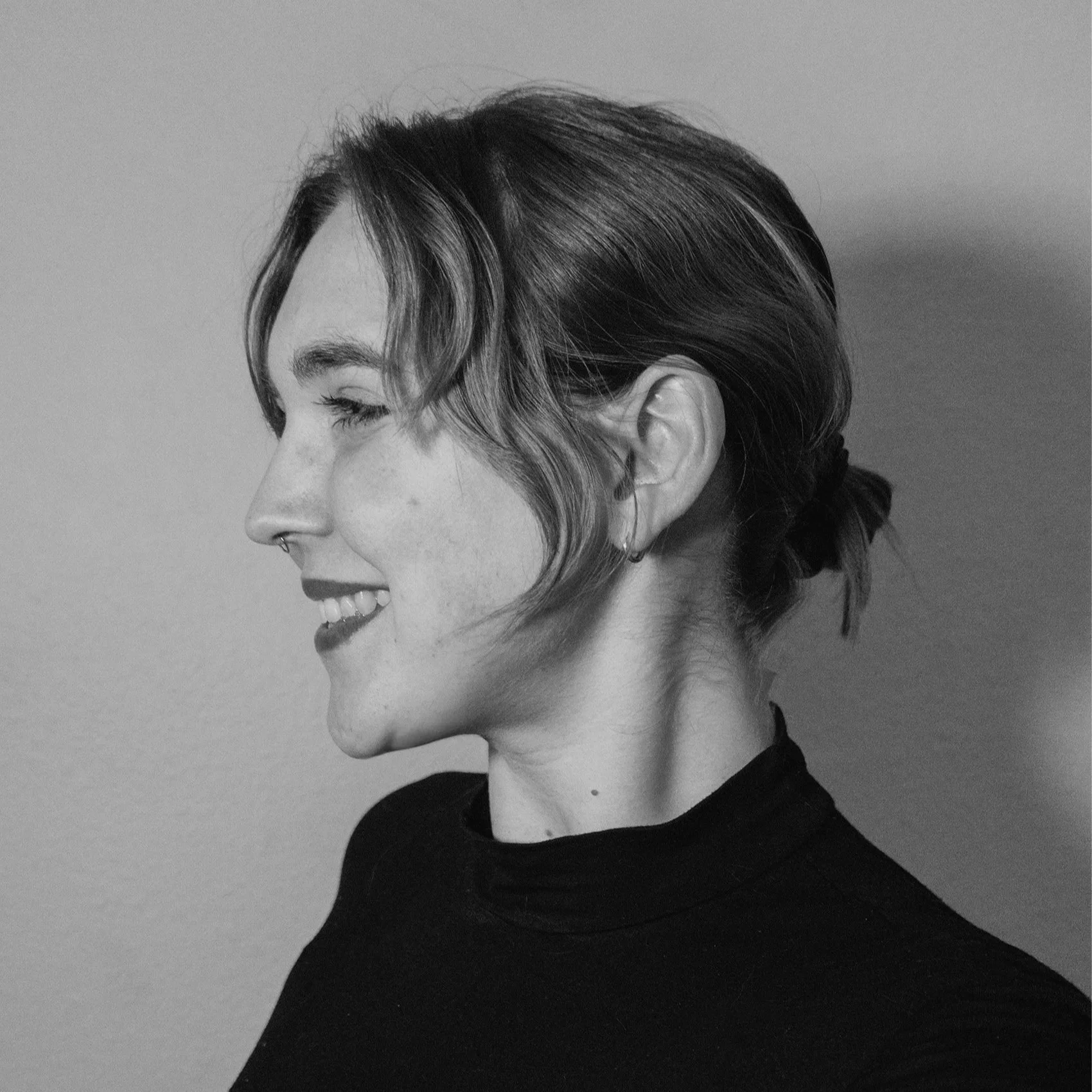 A black and white portrait of a smiling woman with a short, wavy hairstyle, wearing a black top against a plain background.