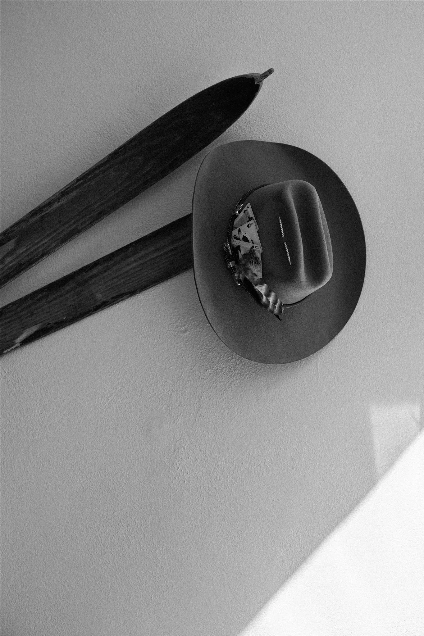 A black object on a wall shelf, with a pack of playing cards, a zipper case, and a straw hat with a hatband casting a shadow on the wall.