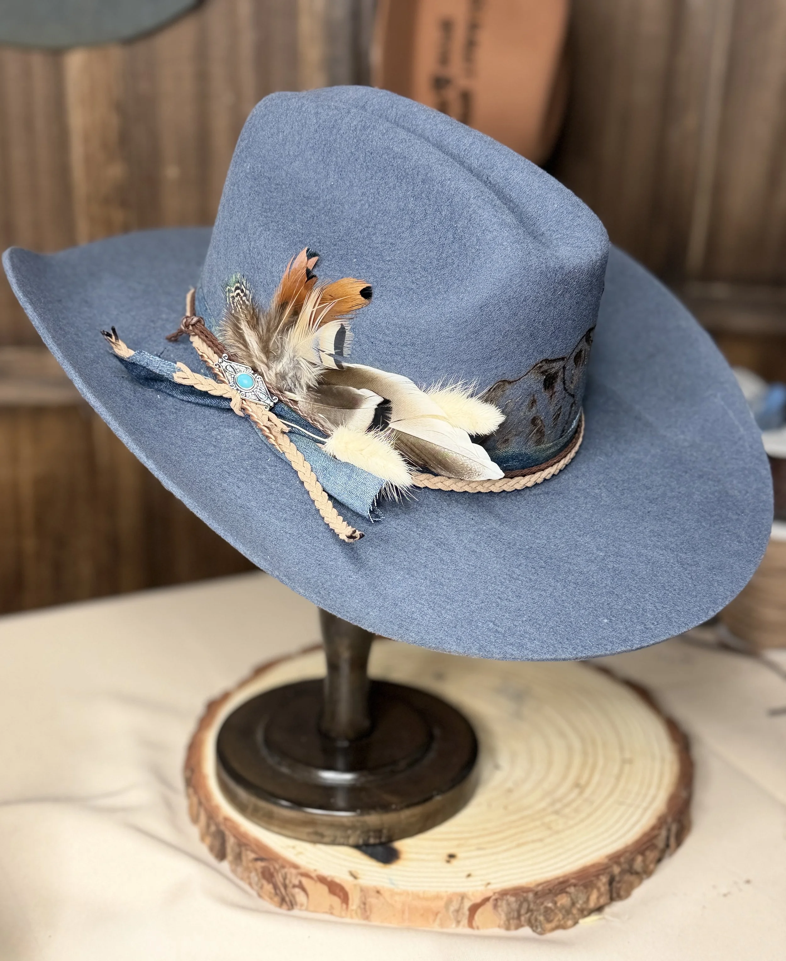 A blue hat decorated with feathers and a decorative pin resting on a wooden log display.