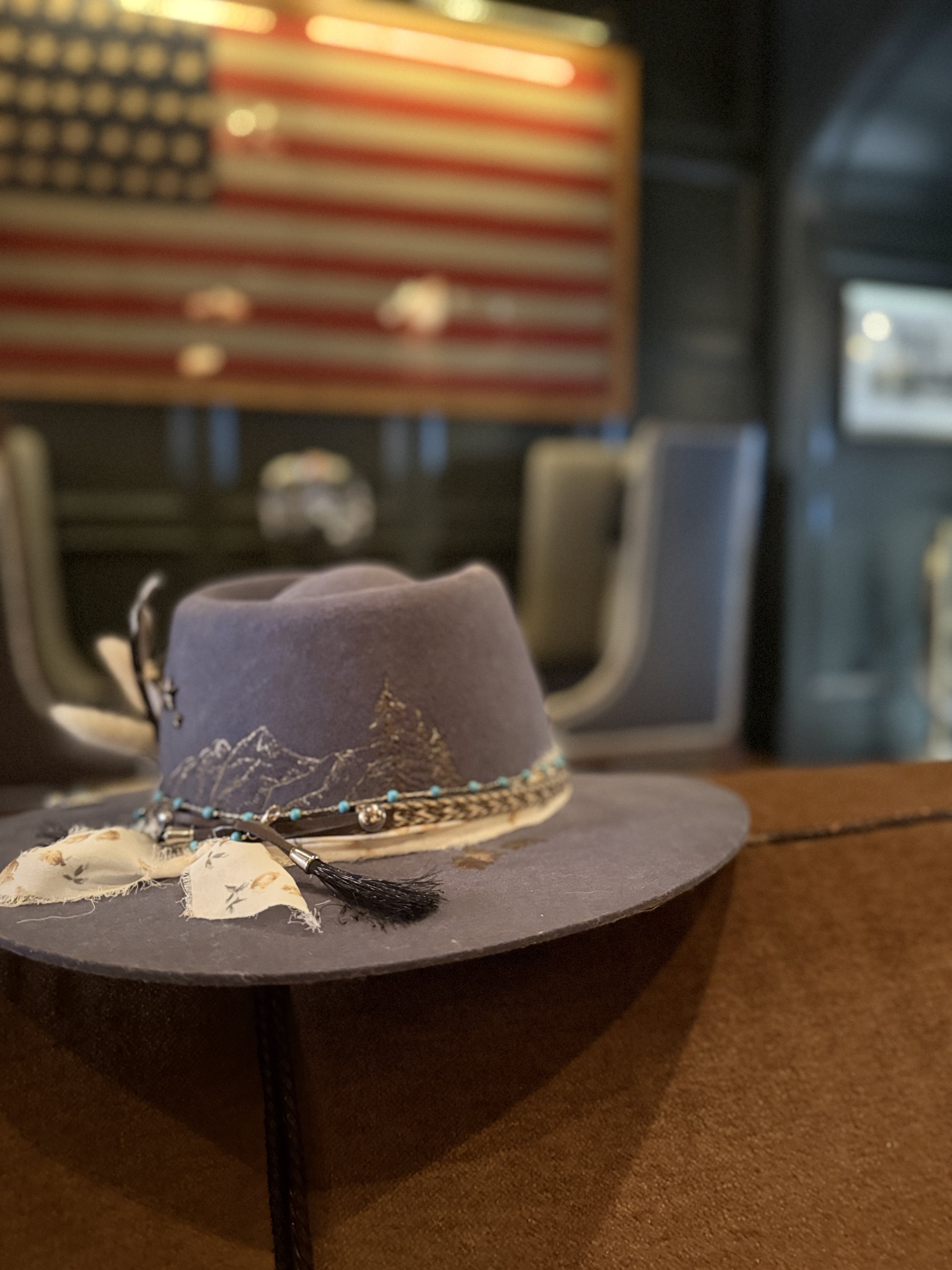 A gray cowboy hat decorated with turquoise beads and a black feather, placed on a dark surface.