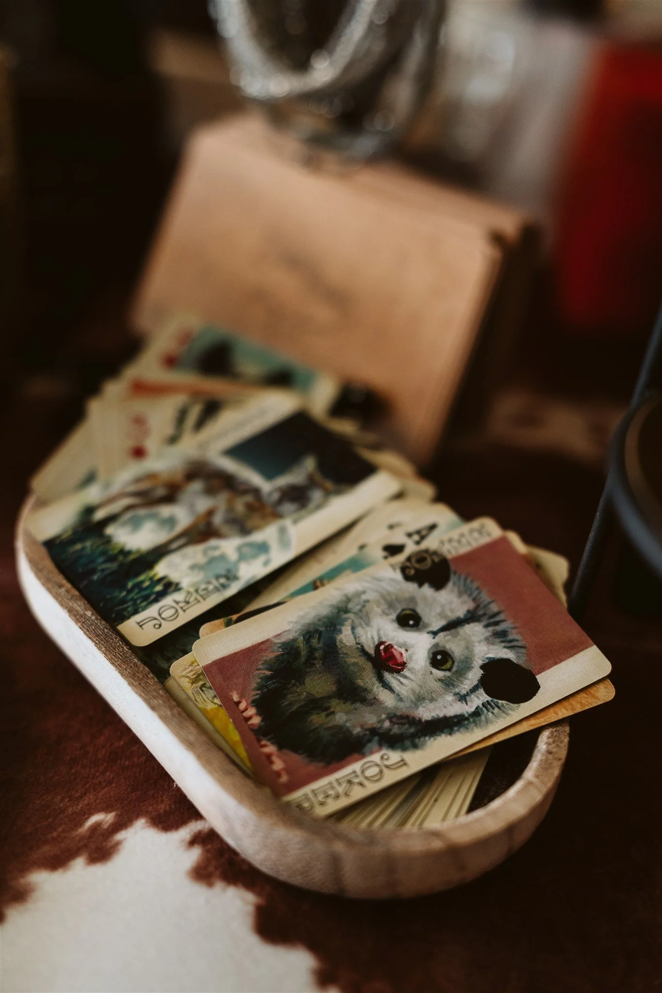 A wooden tray holding various playing cards, including a card with a cute husky dog illustration, on a dark surface with a cowhide pattern.