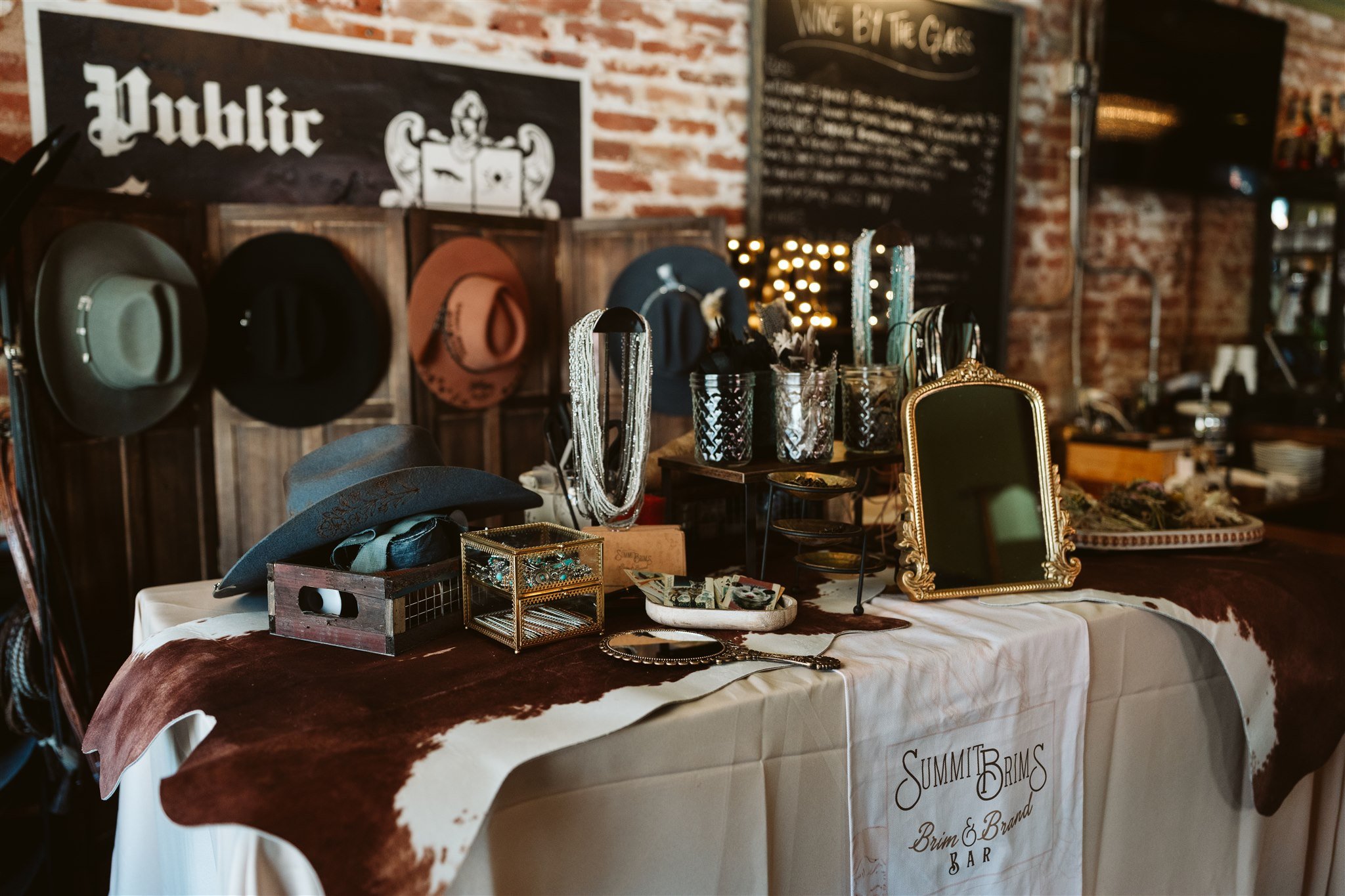 A display table with various accessories including hats, jewelry, and picture frames, set against a brick wall with signs reading 'Public' and other display boards in a vintage or thrift shop.