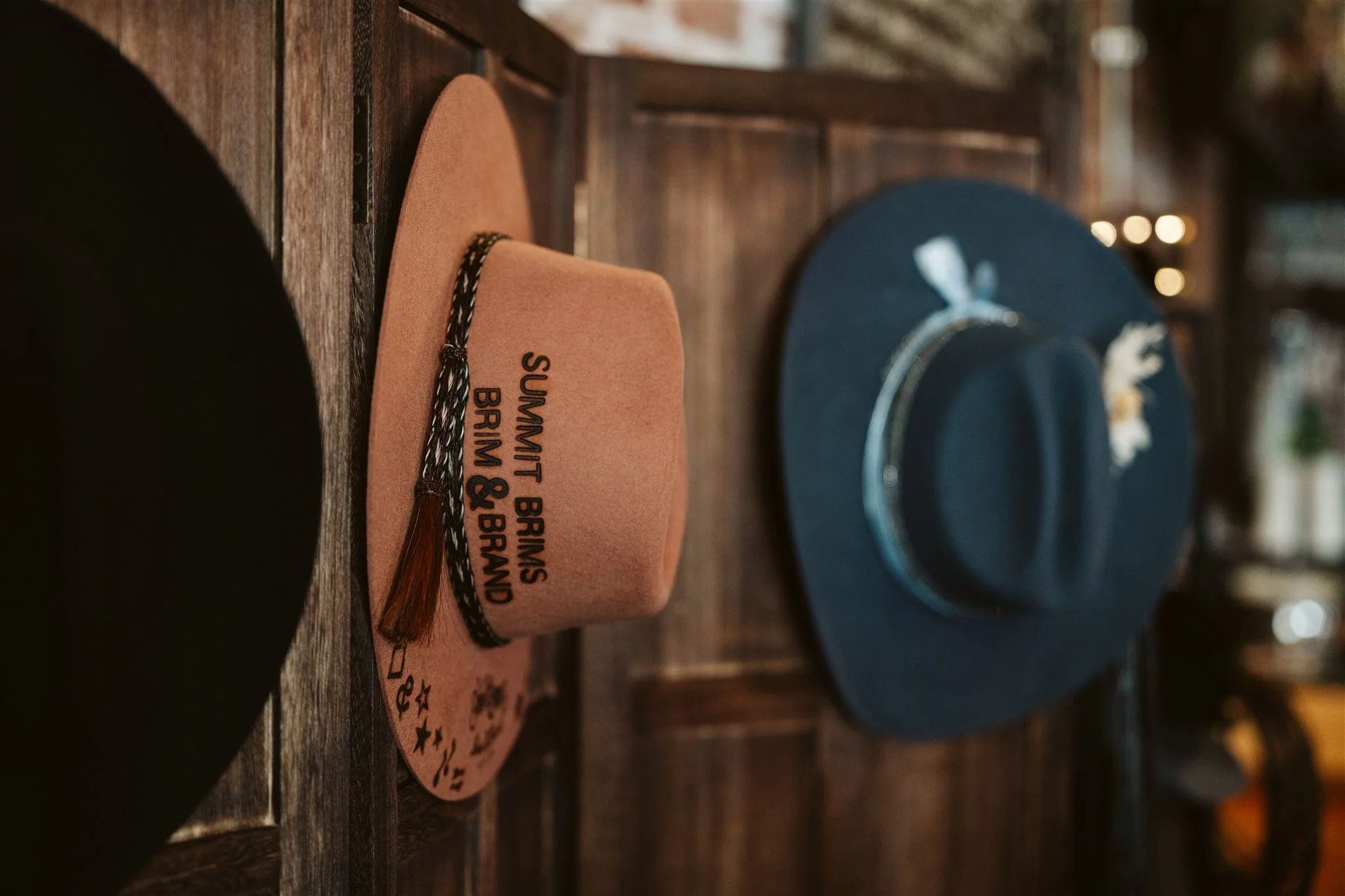 Close-up of a pink felt hat with text and a tassel, and a dark blue hat with a floral decoration, displayed on a wooden surface.