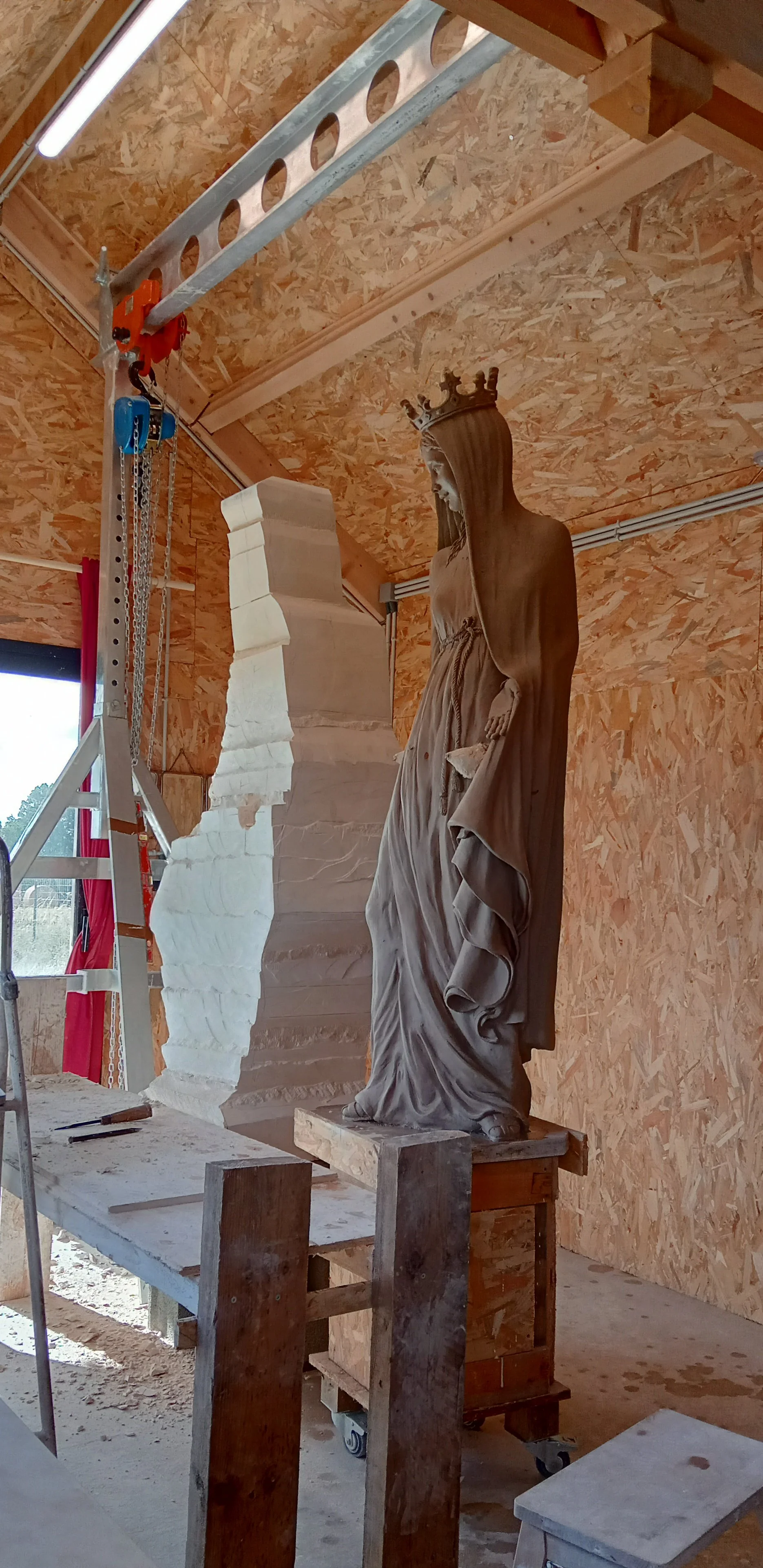 Une sculpture de Vierge Marie en cours de fabrication dans un atelier avec un échafaudage et des outils visibles.
