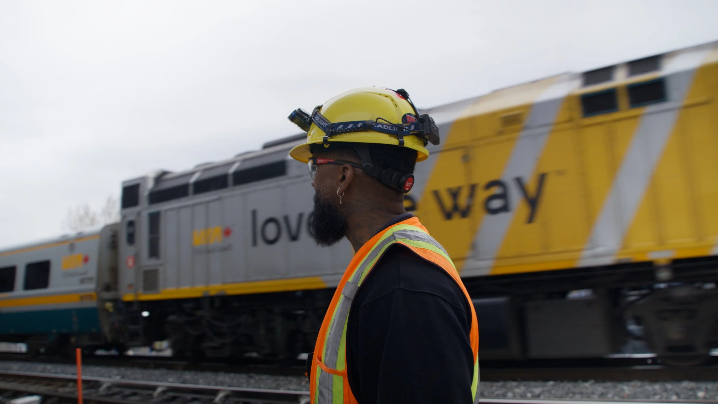 Homme portant un casque de sécurité jaune et un gilet réfléchissant orange, à côté d'un train