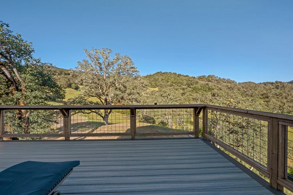 View from a wooden deck overlooking a lush, green hillside with trees and a clear blue sky.