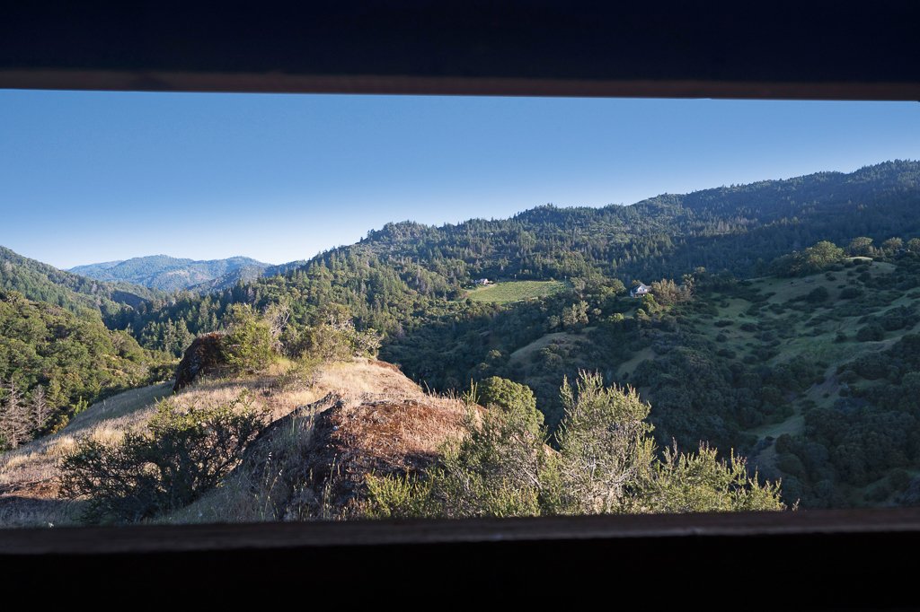 Mountainous landscape with trees and rolling hills, viewed through a window or opening.