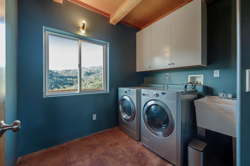 Laundry room with teal walls, a window showing a mountain landscape, white cabinets, a washing machine, a dryer, and a utility sink.