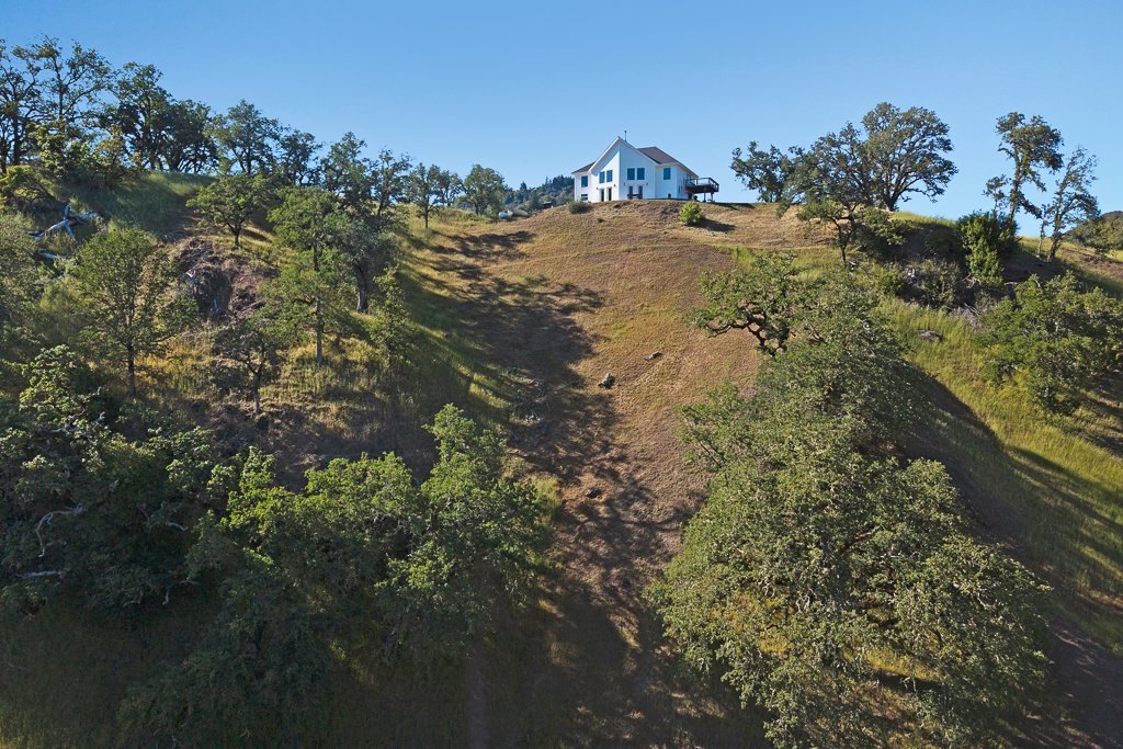 A house on a hill with trees and clear blue sky.