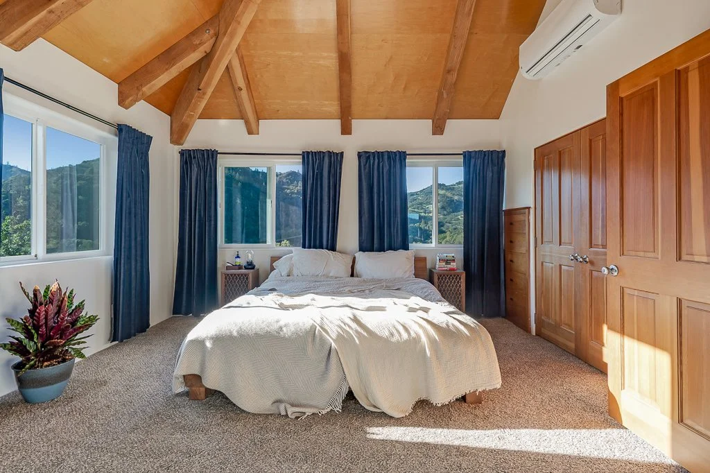 Bedroom with a bed, nightstands, windows with mountain views, wooden ceiling and closet, air conditioning unit, and a potted plant.