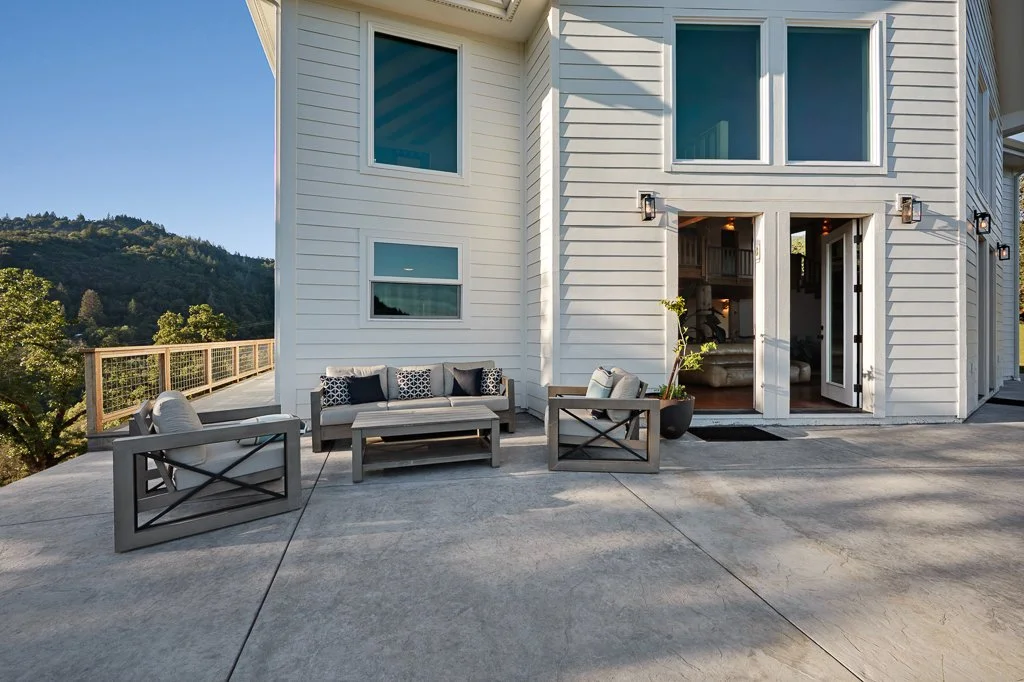 Furniture on an outdoor patio with a view of trees and hills in the background, featuring a sofa, two armchairs, and a potted plant.