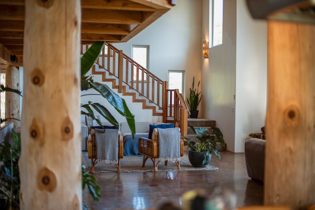 Interior of a house with a staircase, wooden beams, a couch with blankets, and several green potted plants.