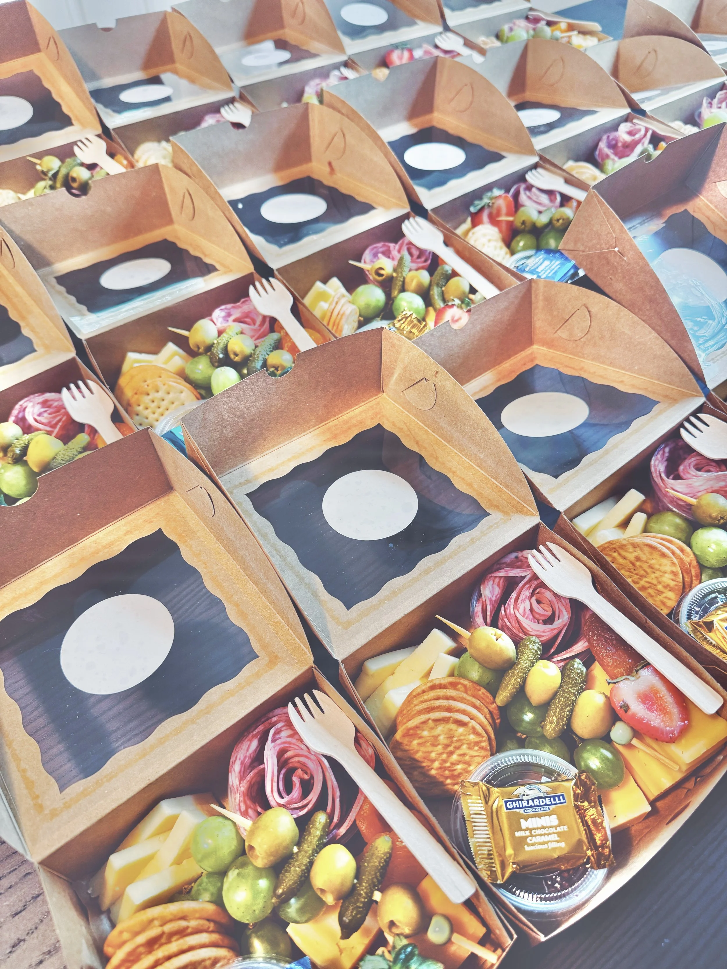 Multiple pizza boxes filled with cheese, vegetables, and snacks, with some chocolate candies and small forks visible.