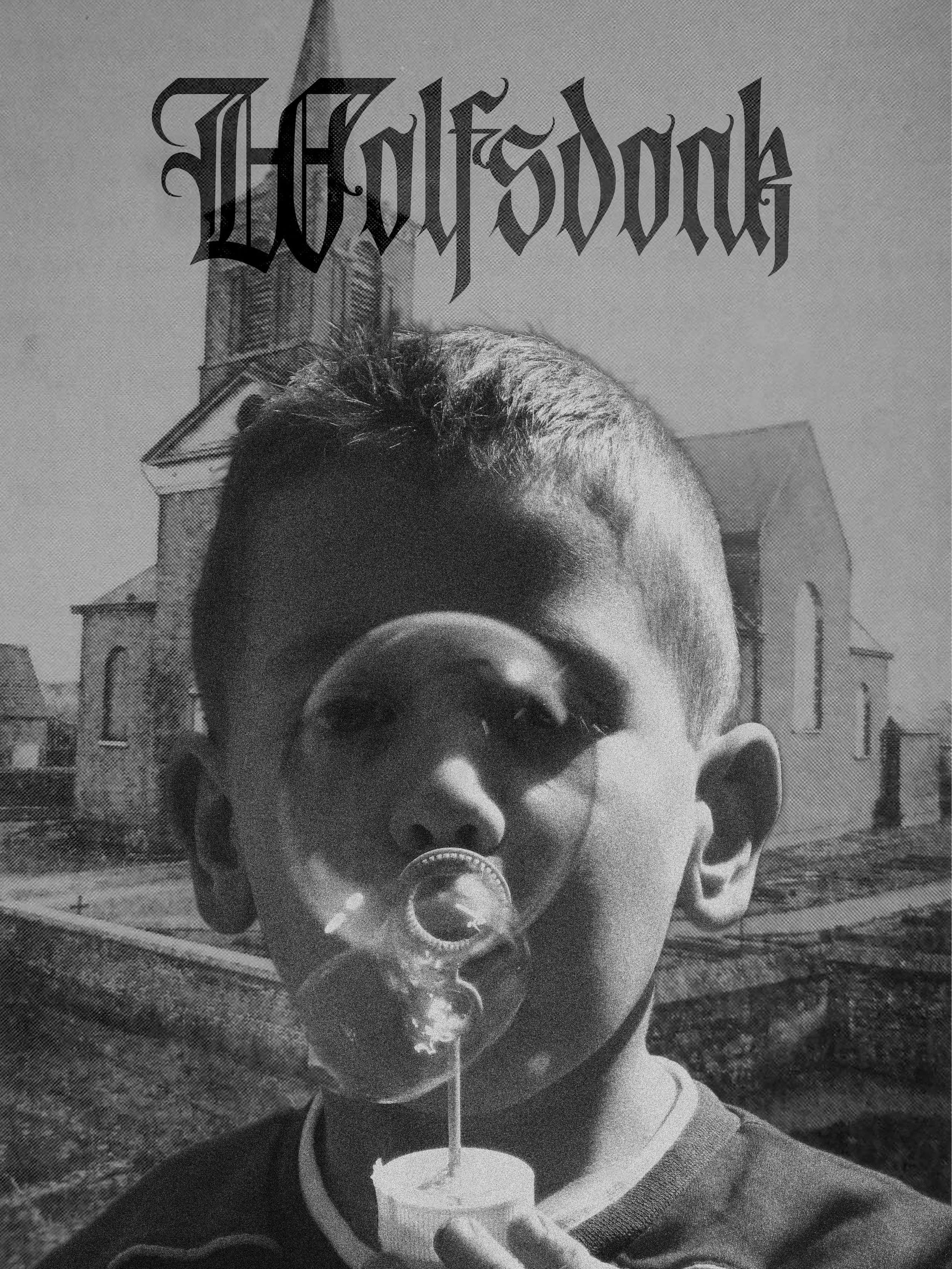 A young boy with short hair is holding a cup with a straw and drinking from it. He is wearing a dark T-shirt with a light-colored collar. In the background, there is a large building resembling a castle or cathedral with towers, and the photo is take