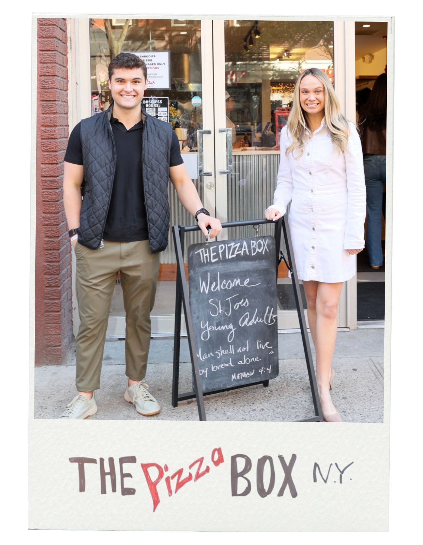 Two smiling people standing outside a pizza shop, with a blackboard sign in front that reads, "Welcome SJ Toss, Young Adults, Man shall not live by bread alone, Matthew 4:4."