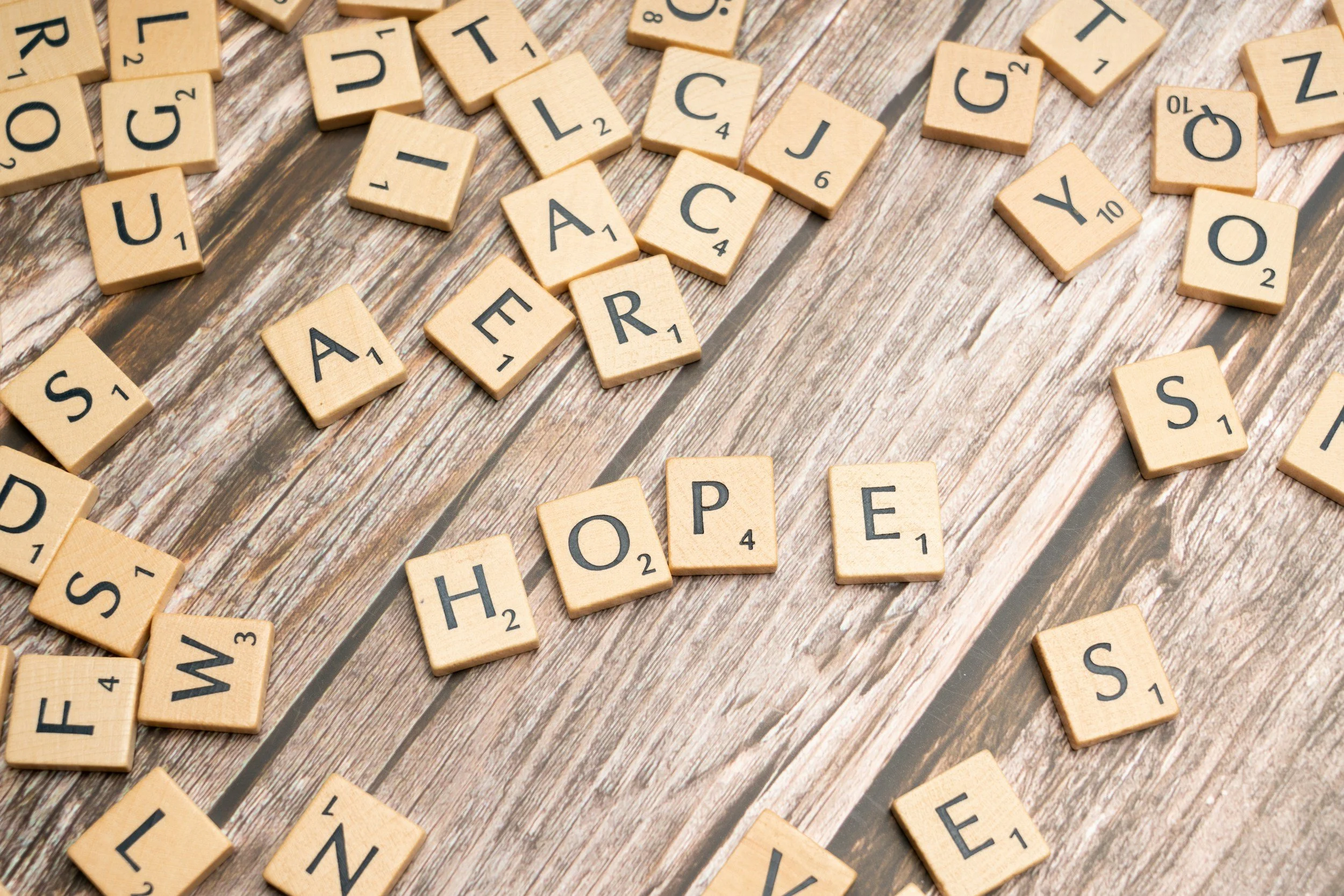 A scattered arrangement of Scrabble letter tiles on a wooden surface, some forming words and others randomly placed.