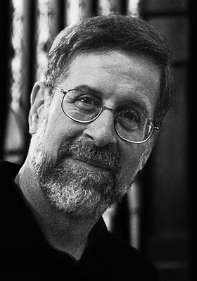 A black-and-white portrait of a middle-aged man with glasses, a beard, and short hair, smiling slightly.
