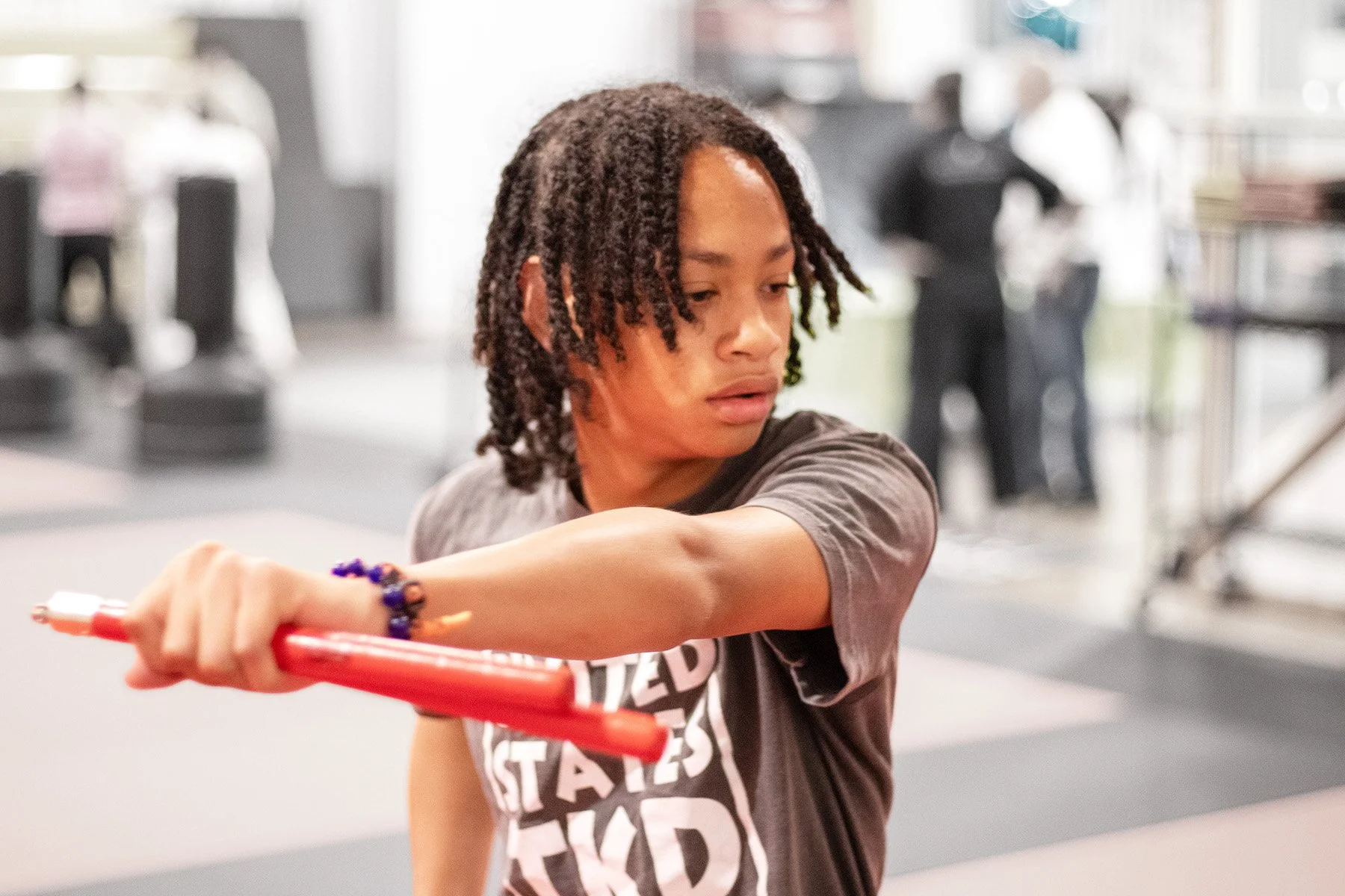 A young man with curly hair trains with red nunchucks during a workout at the martial arts studio.