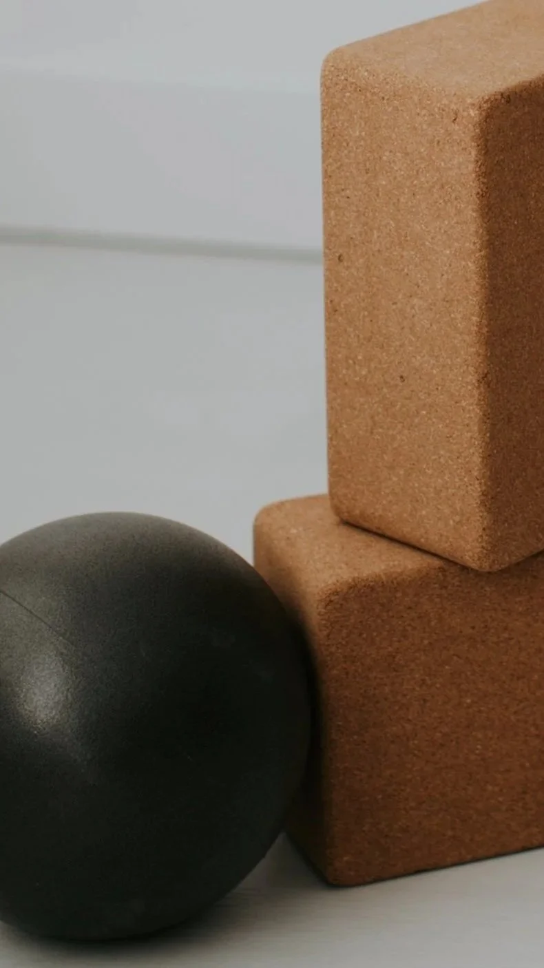 A close-up of two stacked cork yoga blocks and a black exercise ball on a white surface.