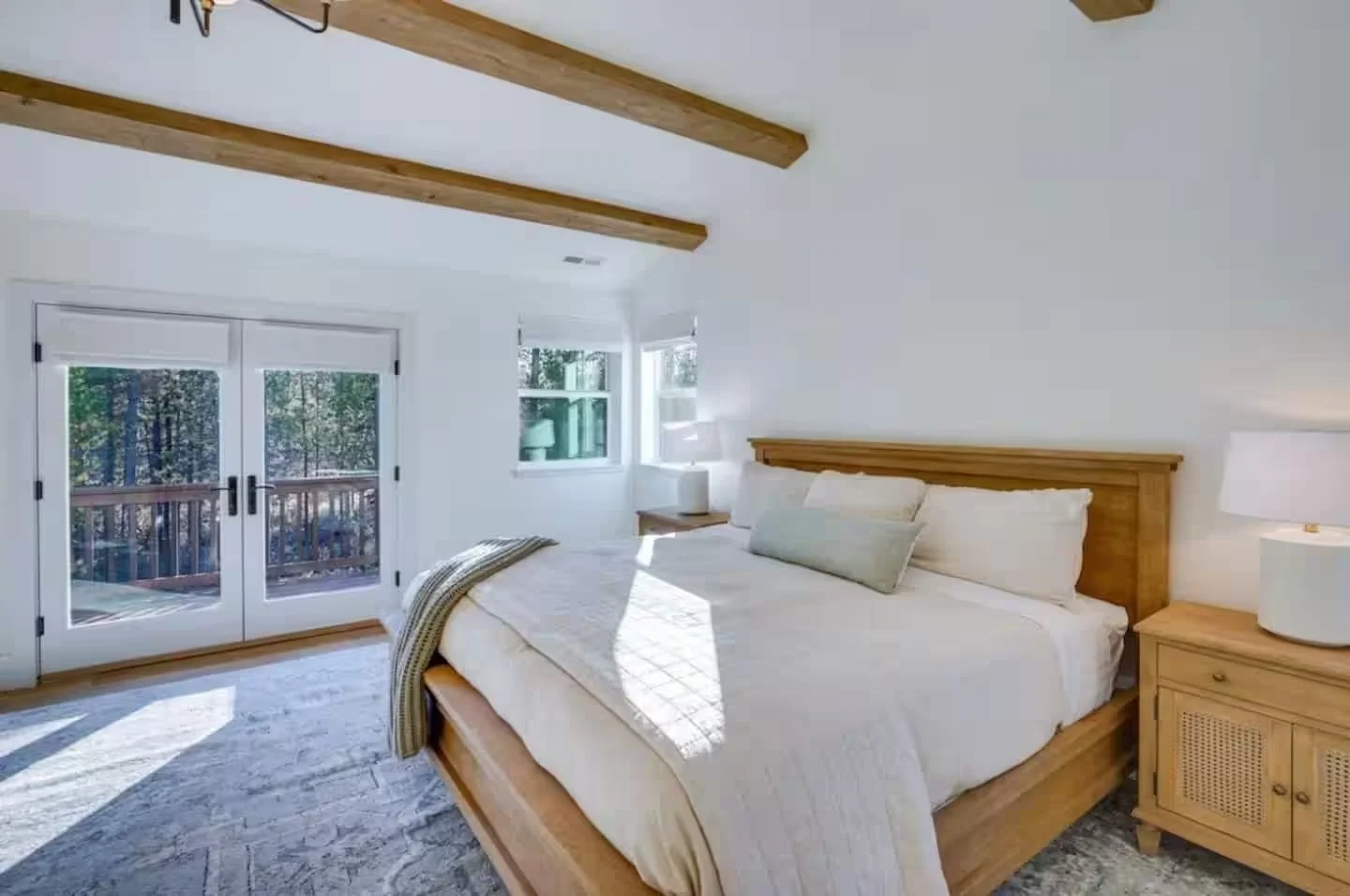 Sunlit bedroom with wood beams and French doors to a deck in the trees