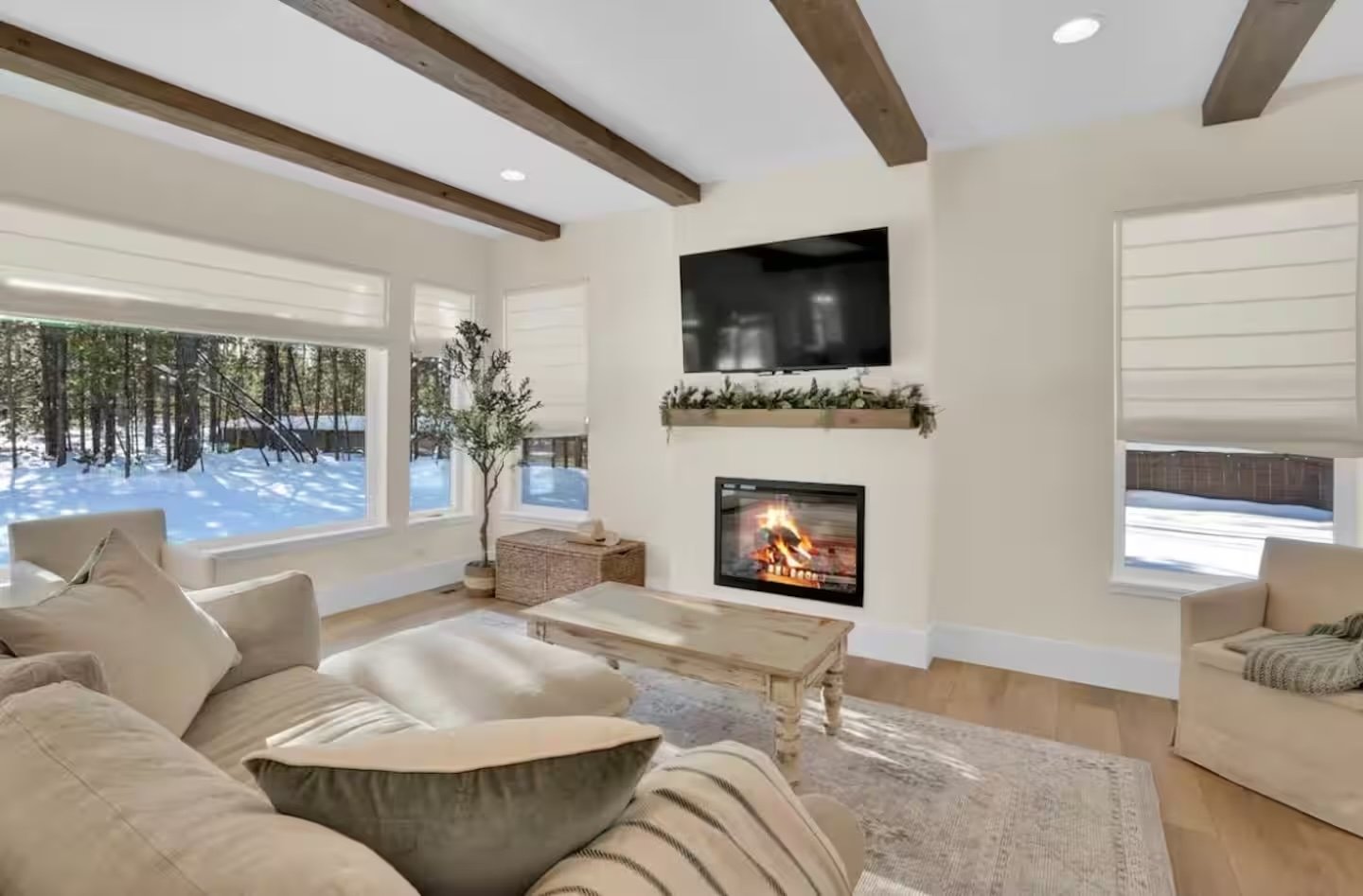 Cozy living room with a lit fireplace, linen sofa and snowy forest view