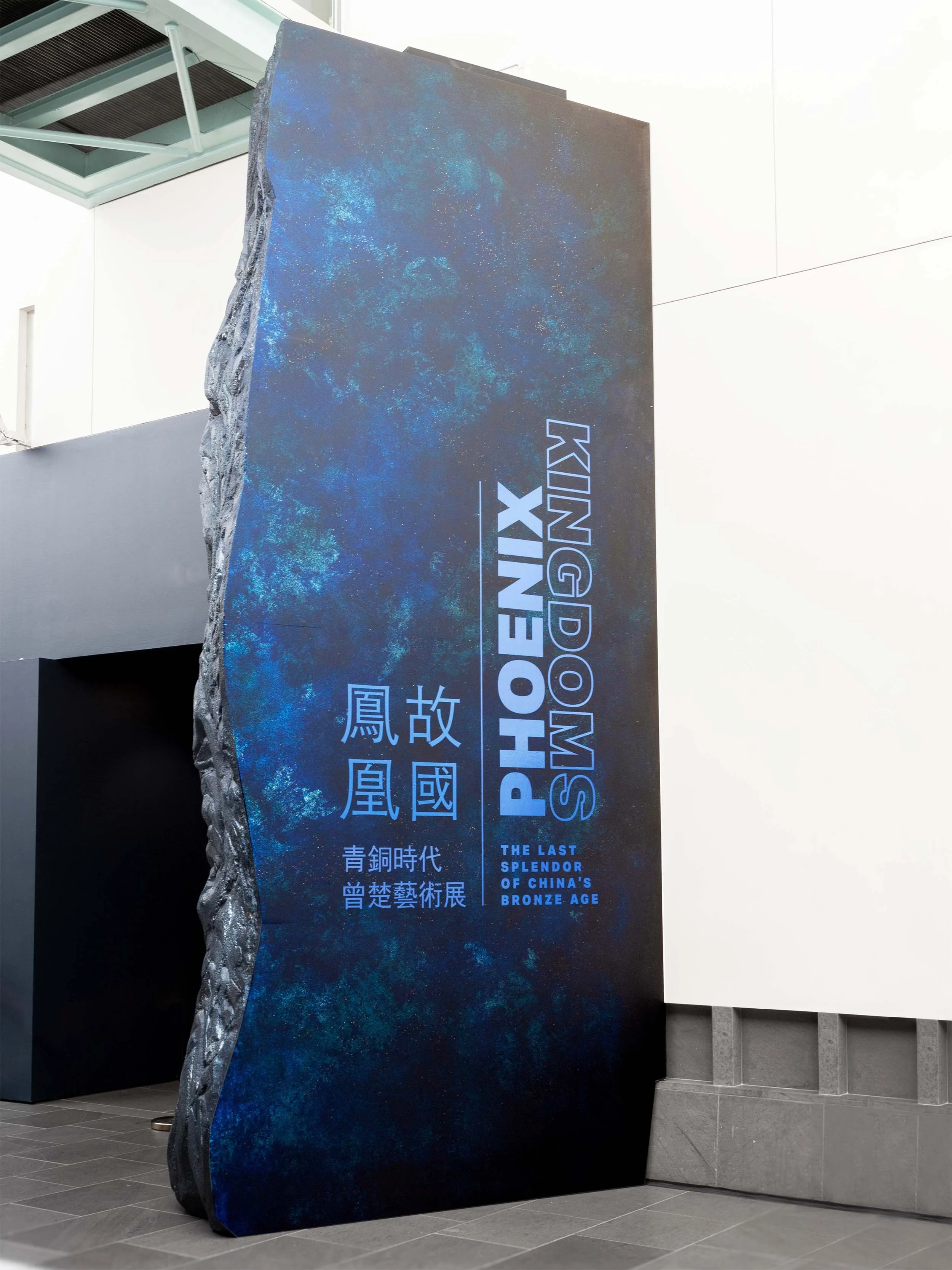 museum exhibition entry to galleries with 30 foot rock wall showing title in English and mandarin