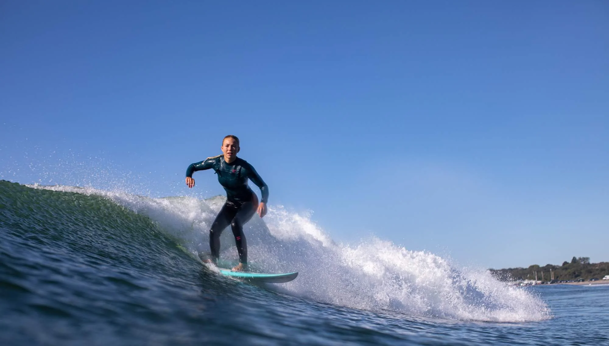 A woman surfing on a wave in the ocean on a clear day with a blue sky.