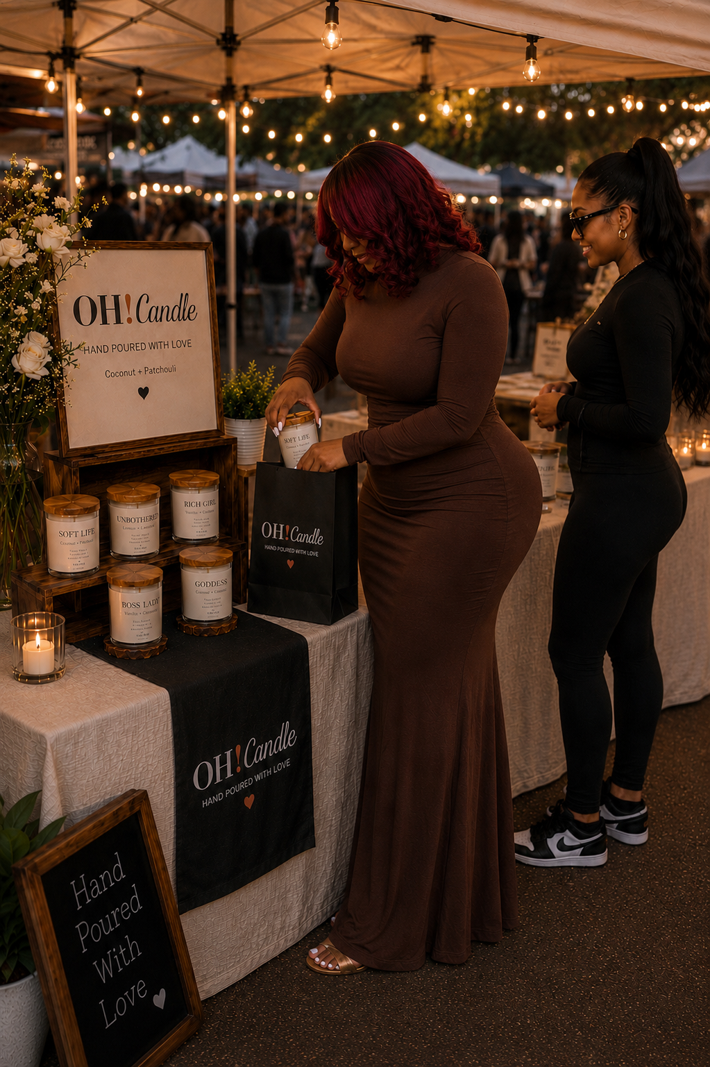 Two women at a candle booth at an outdoor market during the evening. One woman is selecting a candle while the other watches. The booth has a sign that says 'OH! Candle, Hand Poured with Love, Coconut + Patchouli' and various candles displayed on the table. String lights are hanging overhead, creating a warm ambiance.