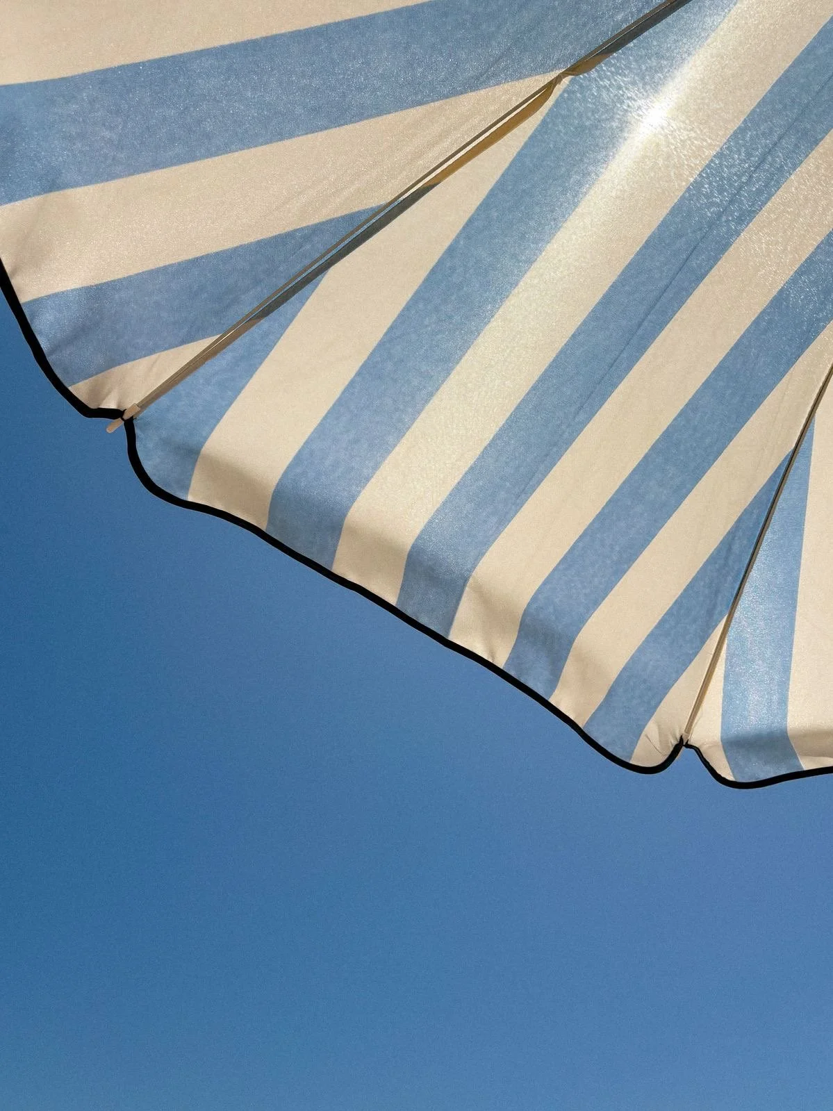 Blue and white striped beach umbrella against a bright blue sky.