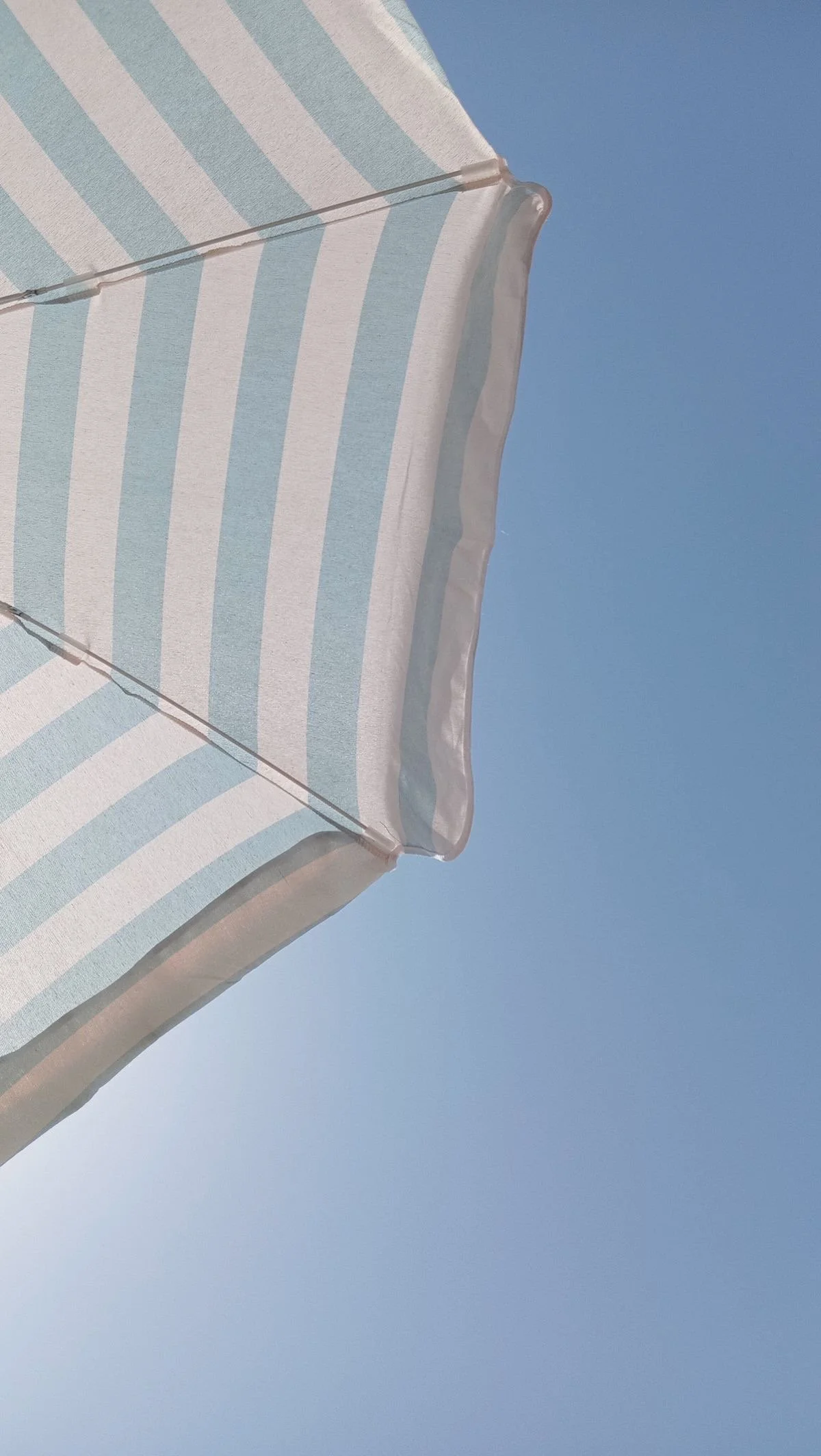 Close-up of a light blue and white striped beach umbrella against a clear blue sky.