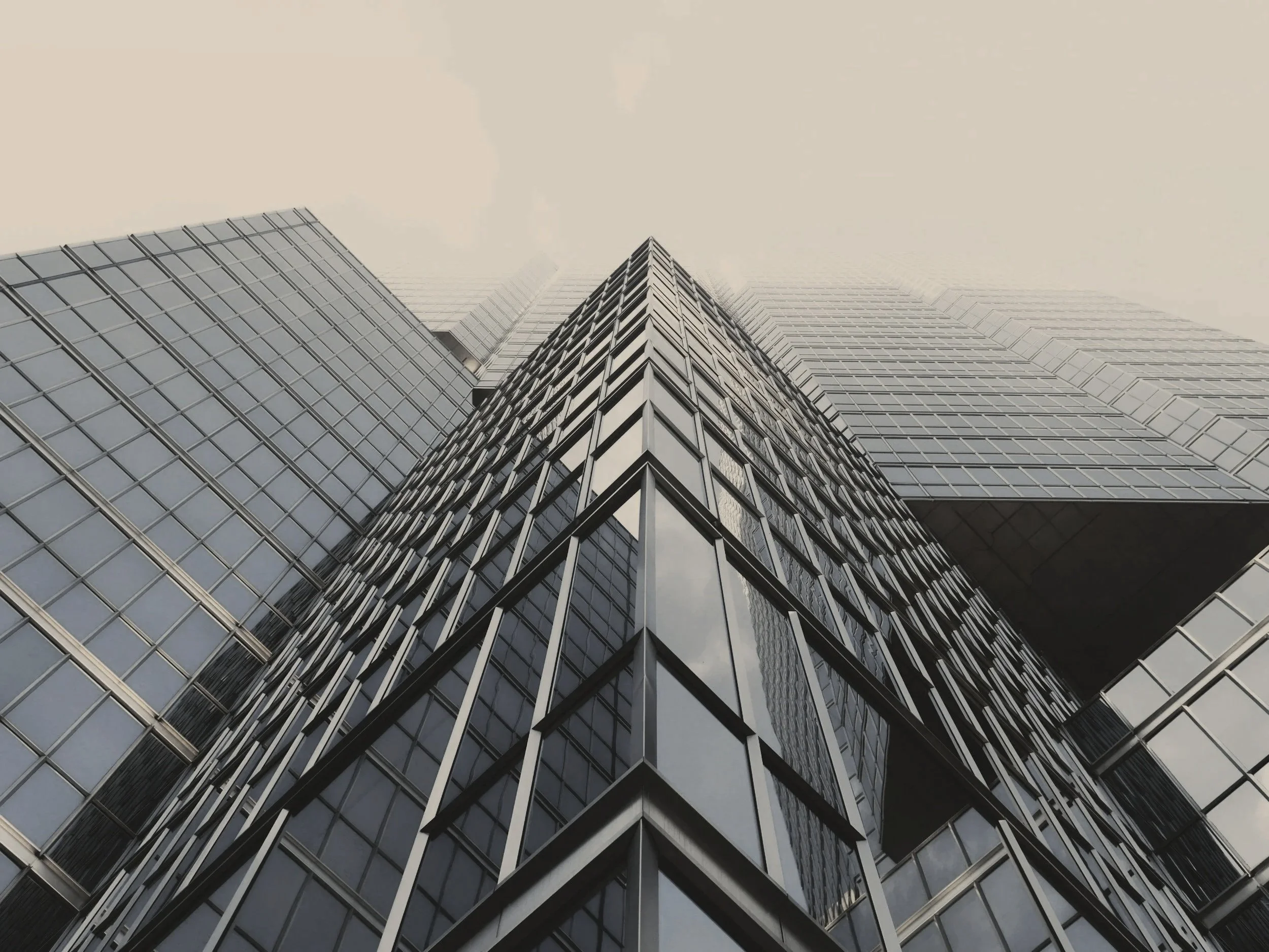 Low-angle shot of a modern skyscraper with reflective glass windows, looking upward towards a cloudy sky.