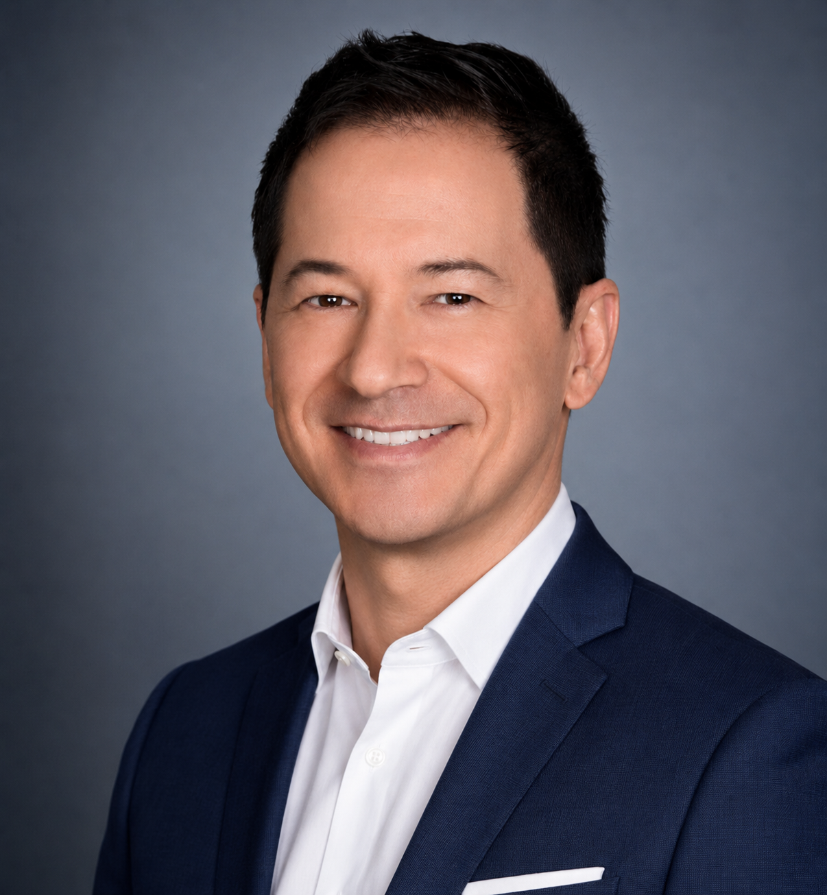 Professional headshot of a smiling man in a dark blue suit and white shirt against a gray background.