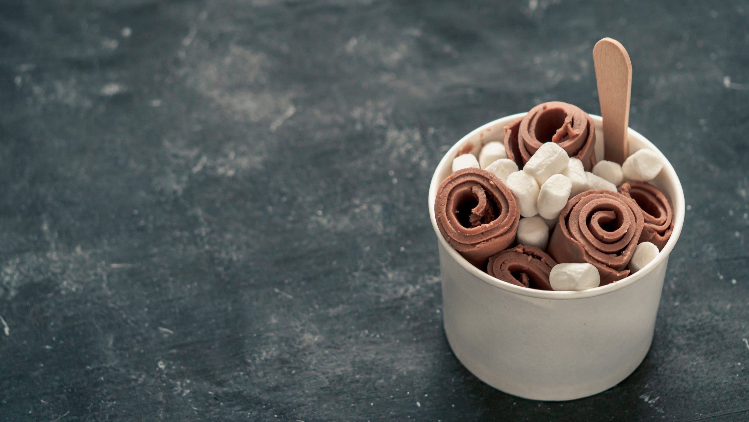 A cup filled with rolled chocolate and white marshmallows, with a small wooden spoon sticking out.