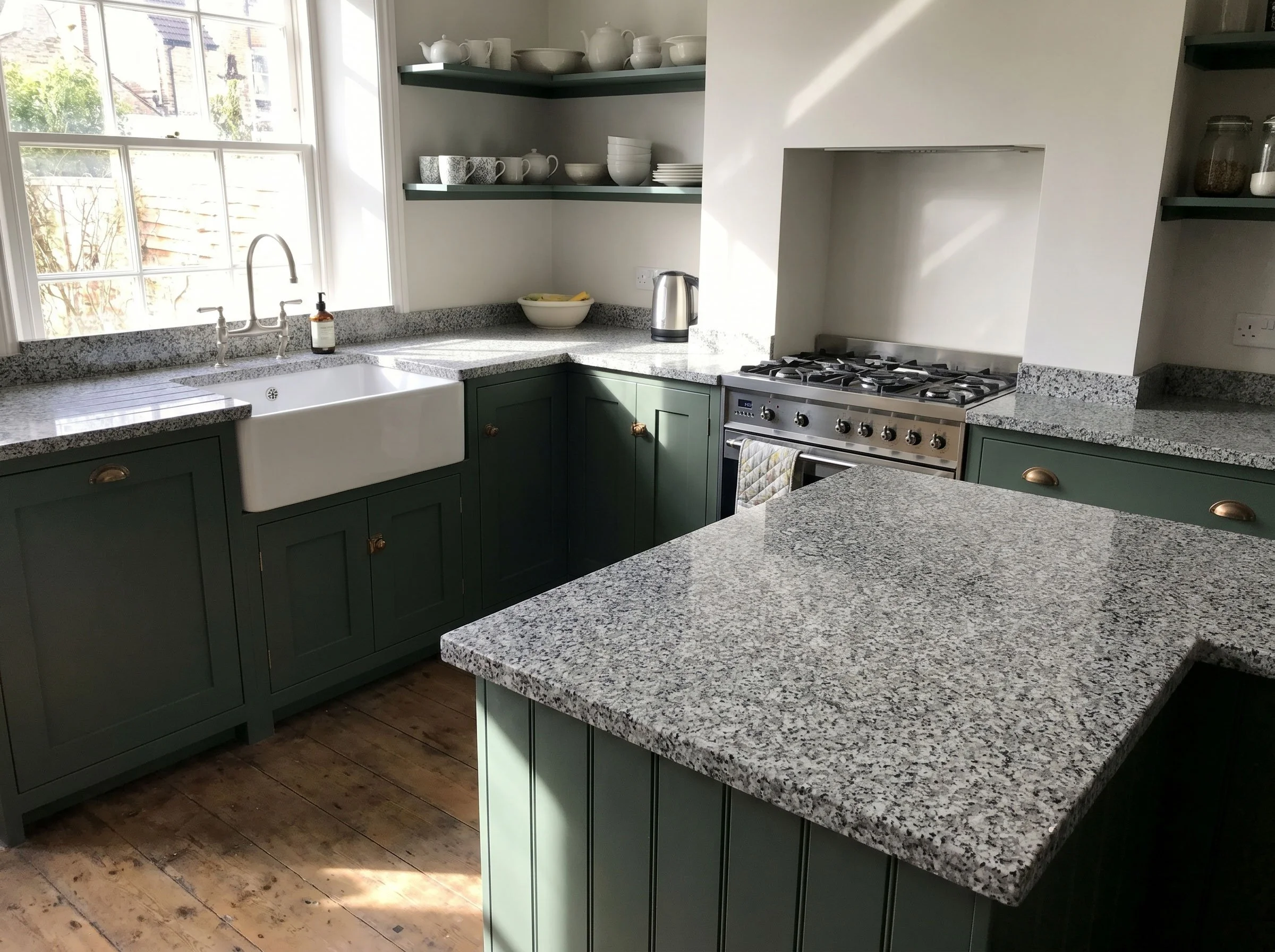 A bright kitchen with green cabinets, granite countertops, a farmhouse sink, stainless steel stove, open shelves with dishes, and wooden flooring.