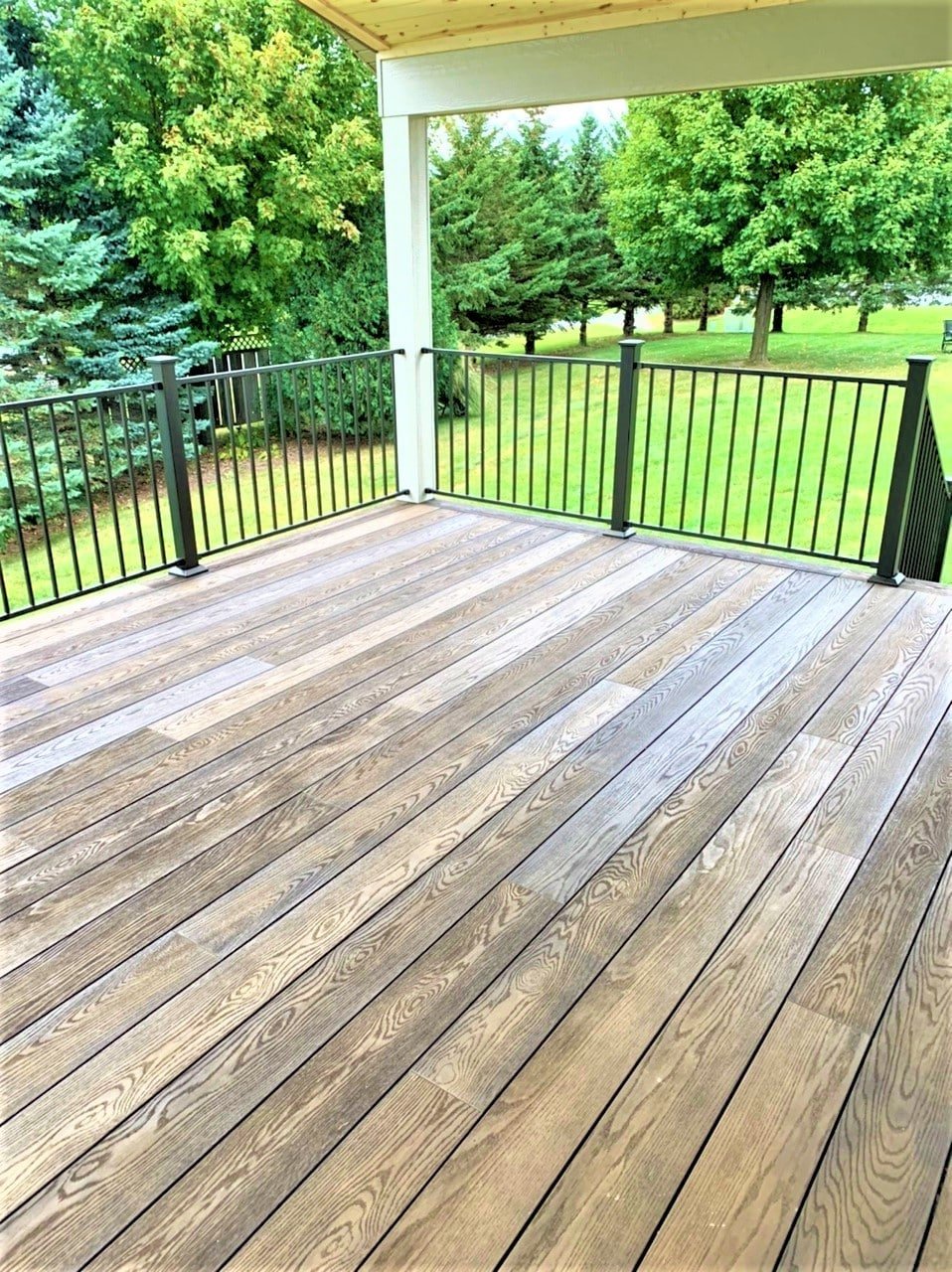 Wooden deck with black metal railing overlooking a green lawn and trees