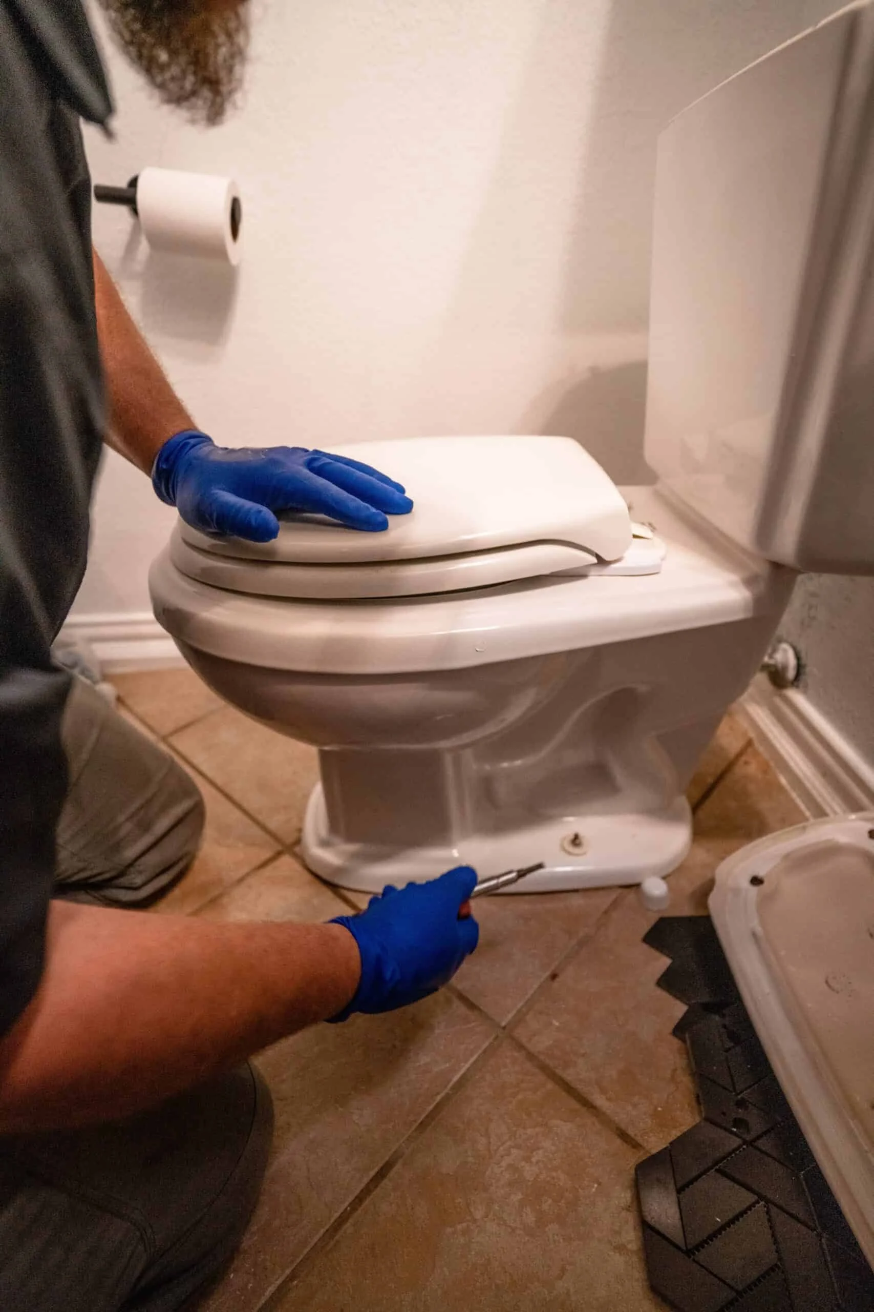 Person with gloves working on a disassembled toilet in a bathroom, with tools nearby.