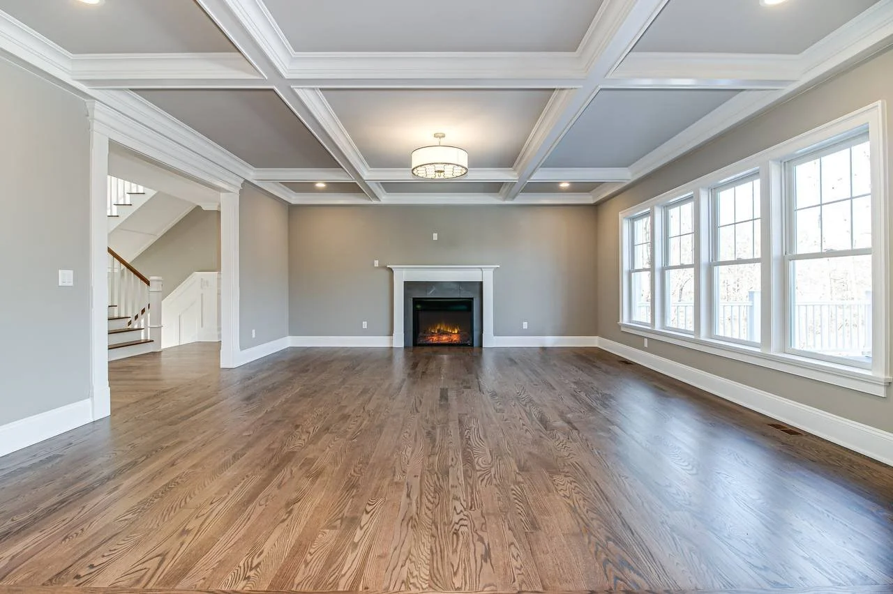 Empty living room with hardwood floors, a fireplace, large windows, and ceiling moldings.