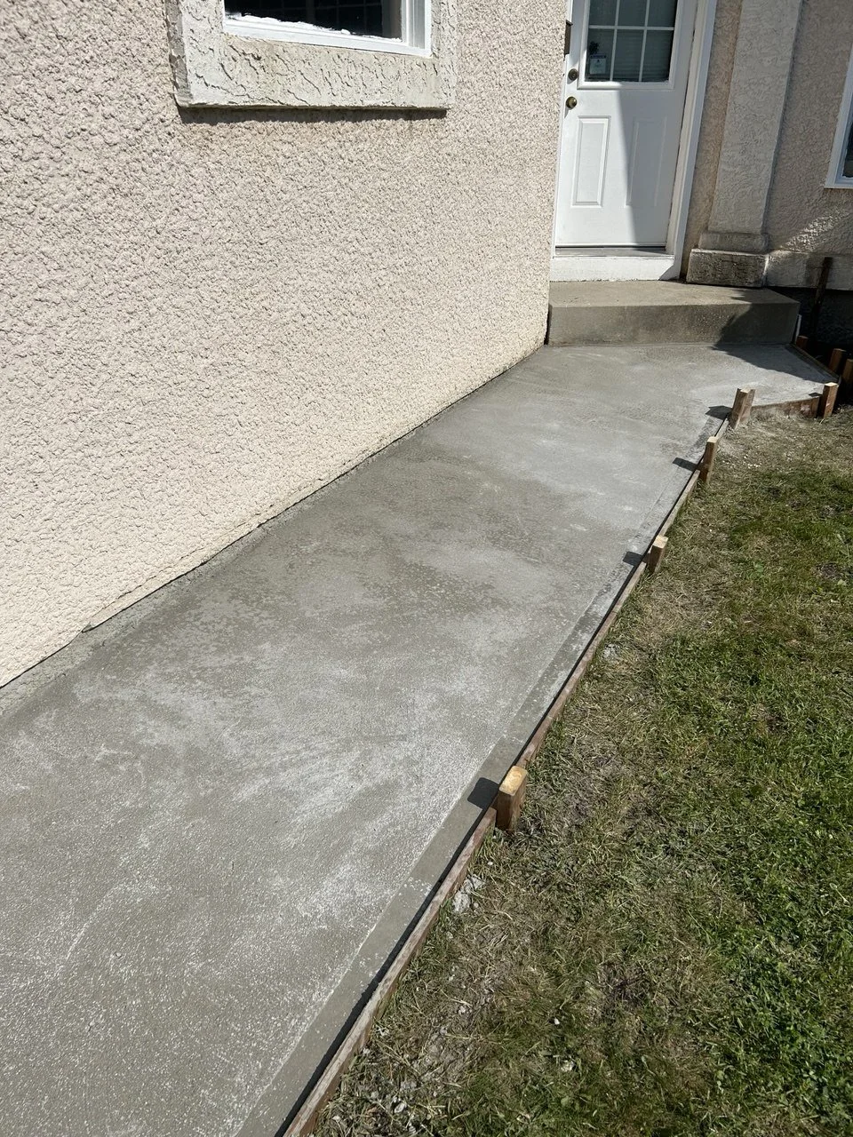 Freshly poured concrete sidewalk along the house exterior, with wooden form boards in place.
