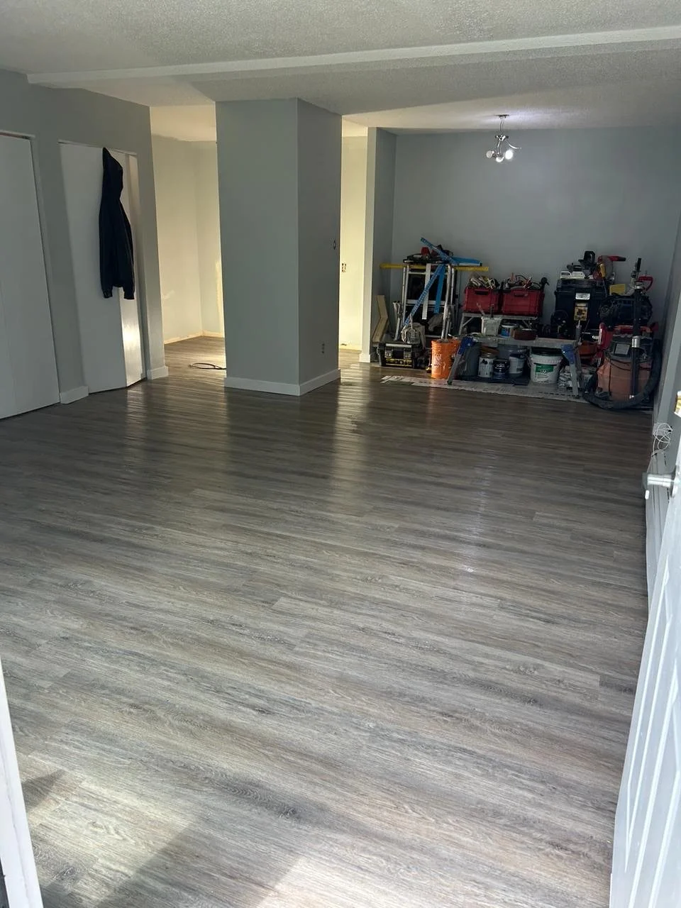 An empty room with new gray wood laminate flooring and a small workspace with tools and supplies in the corner.