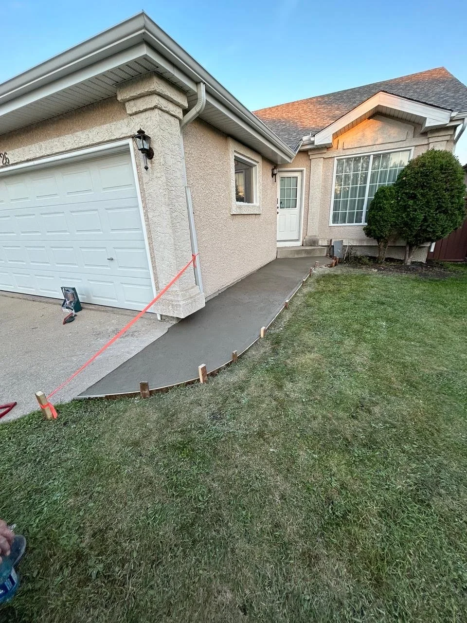 Newly poured concrete walkway in front of house with wooden forms on grass.