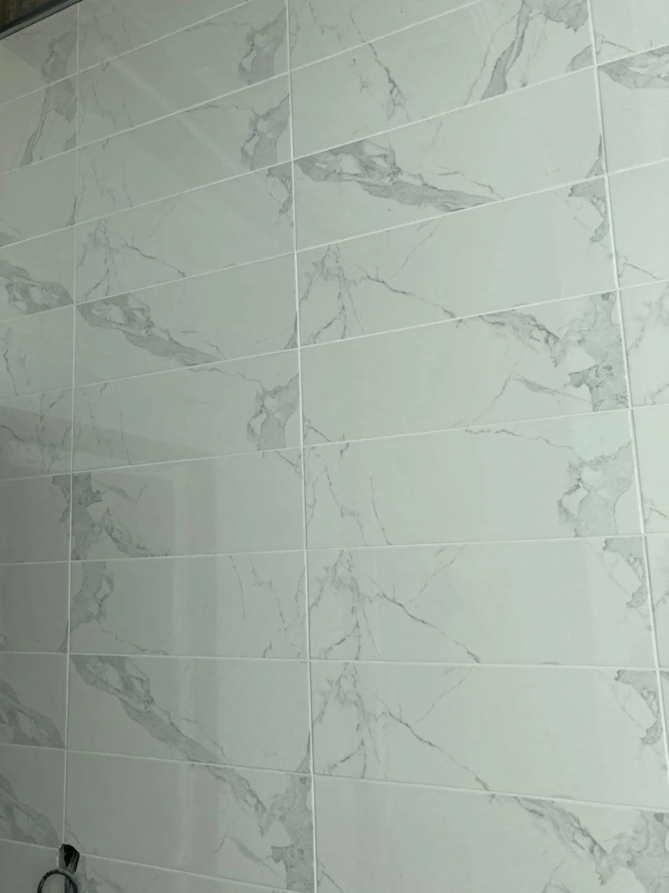 Close-up of a wall with large white marble-patterned ceramic tiles.