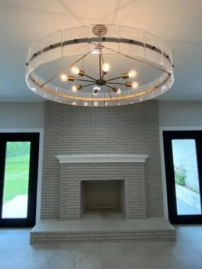 Modern living room with a brick fireplace, two black framed glass doors on either side, and a large circular chandelier hanging from the ceiling.