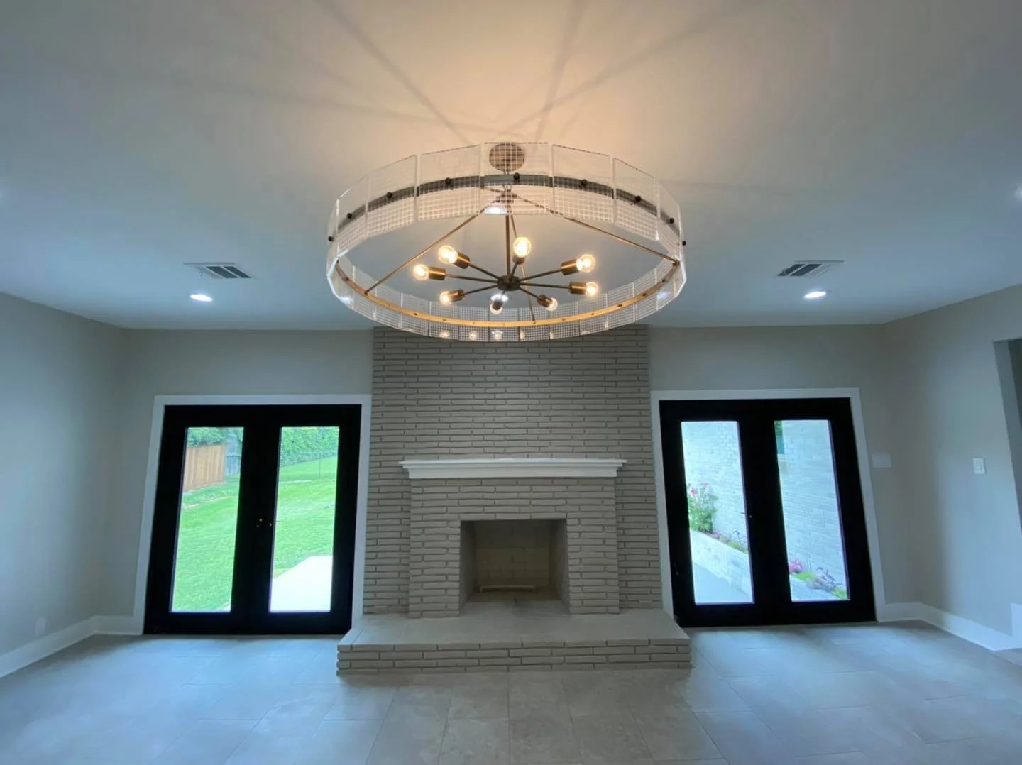 Living room with a modern chandelier, brick fireplace, and sliding glass doors leading to the yard.